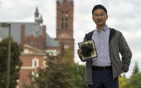 A man standing in front of a brick building, holding a burnt material.