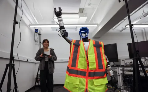 A woman standing behind a robot.