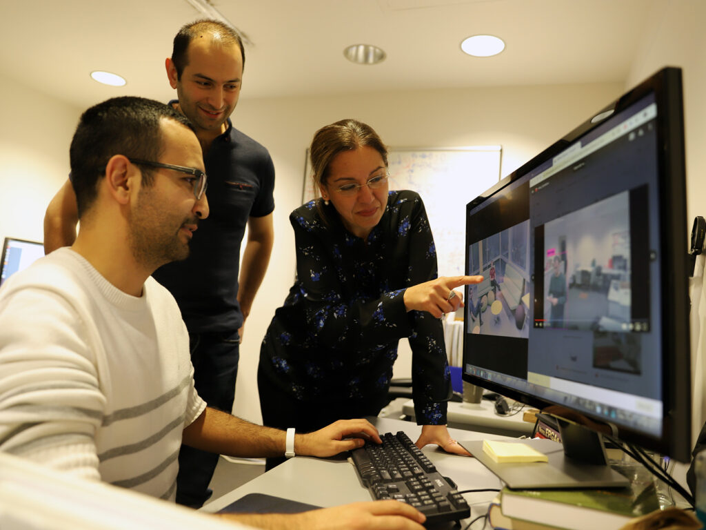 Senem Velipasalar with two PhD students pointing at a computer monitor