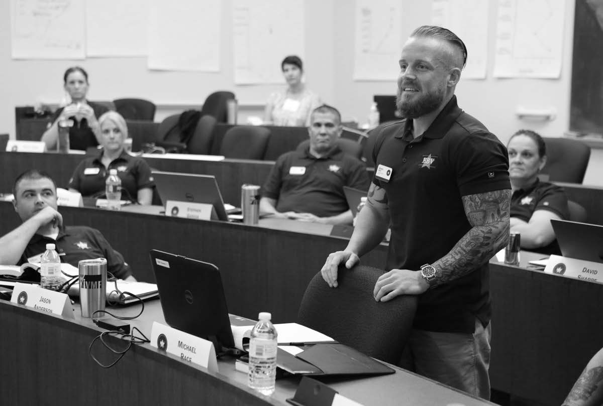Veteran standing in classroom with laptop and other students listening to him speak