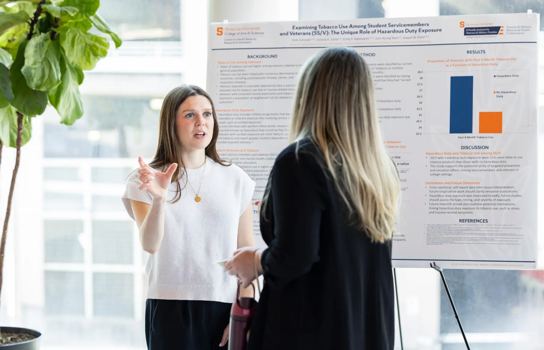 A woman standing in front of a research poster talks intently with another woman near the poster.