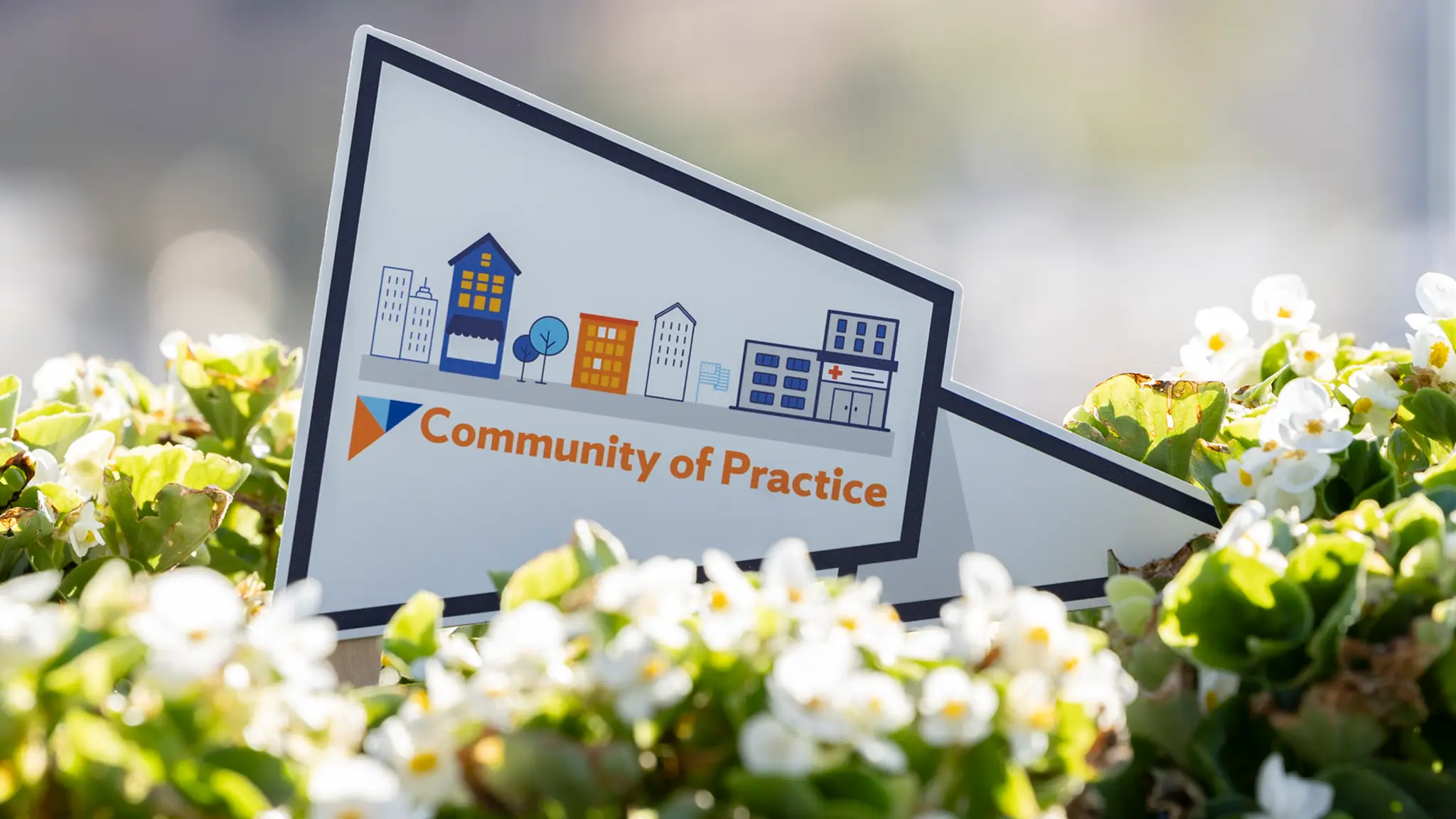 A 2026 Community of Practice graphic card shaped like a triangular pennant caps a large, vibrant bunch of white flowers and greenery.