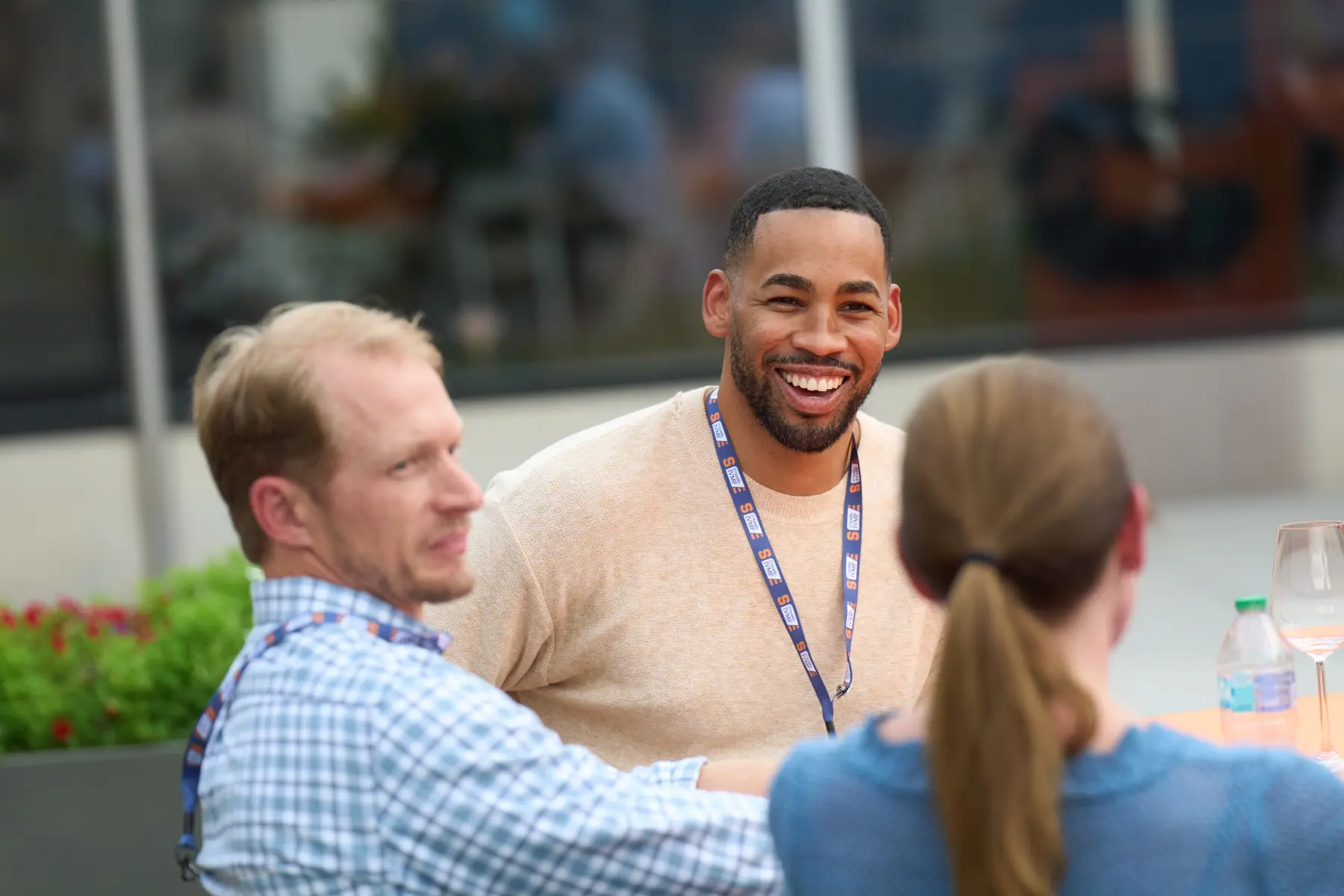 A smiling man looks across the table at a woman. Another man a the table also looks at the same woman.