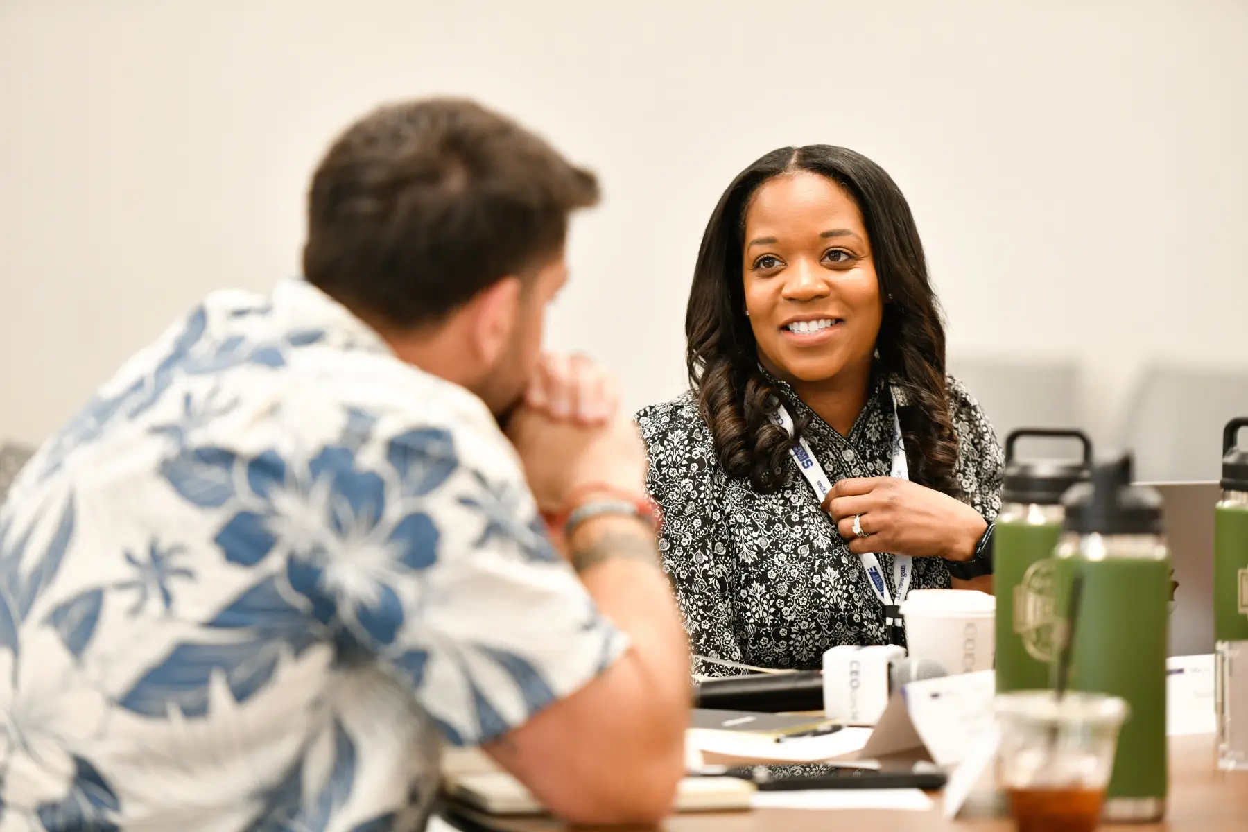 A woman sitting at a table talking with a man a couple seats away.