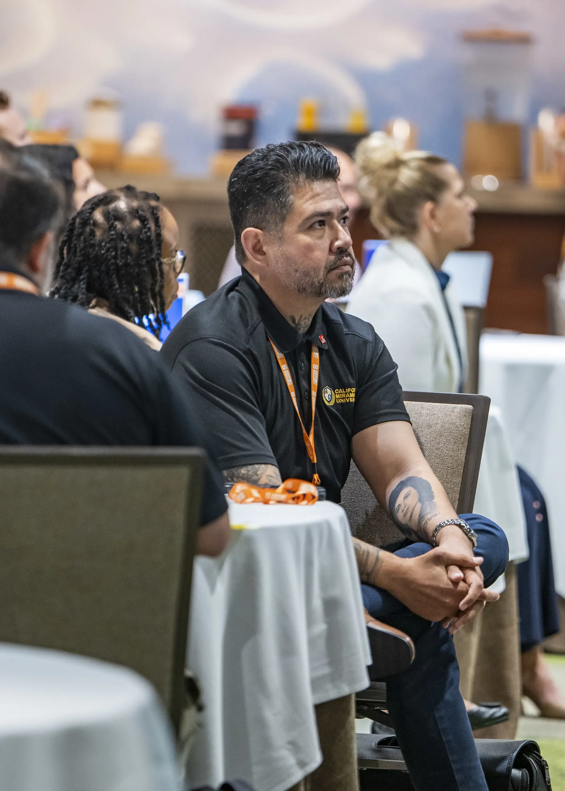 A man attending an IVMF event sits sideways in his chair at a table to focus on the presentation.