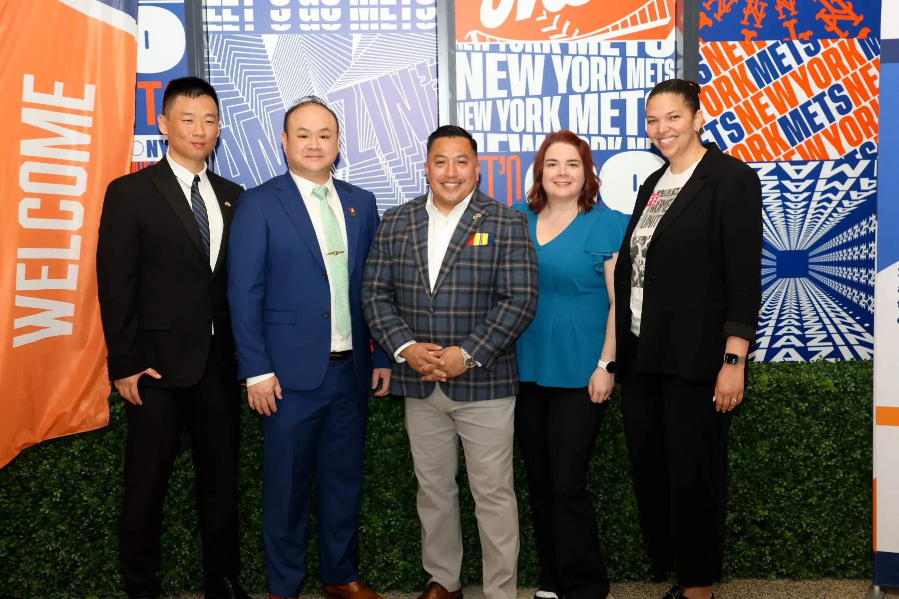Five MEF NYC attendees stand together in front of NY Mets themed posters and fake hedge.