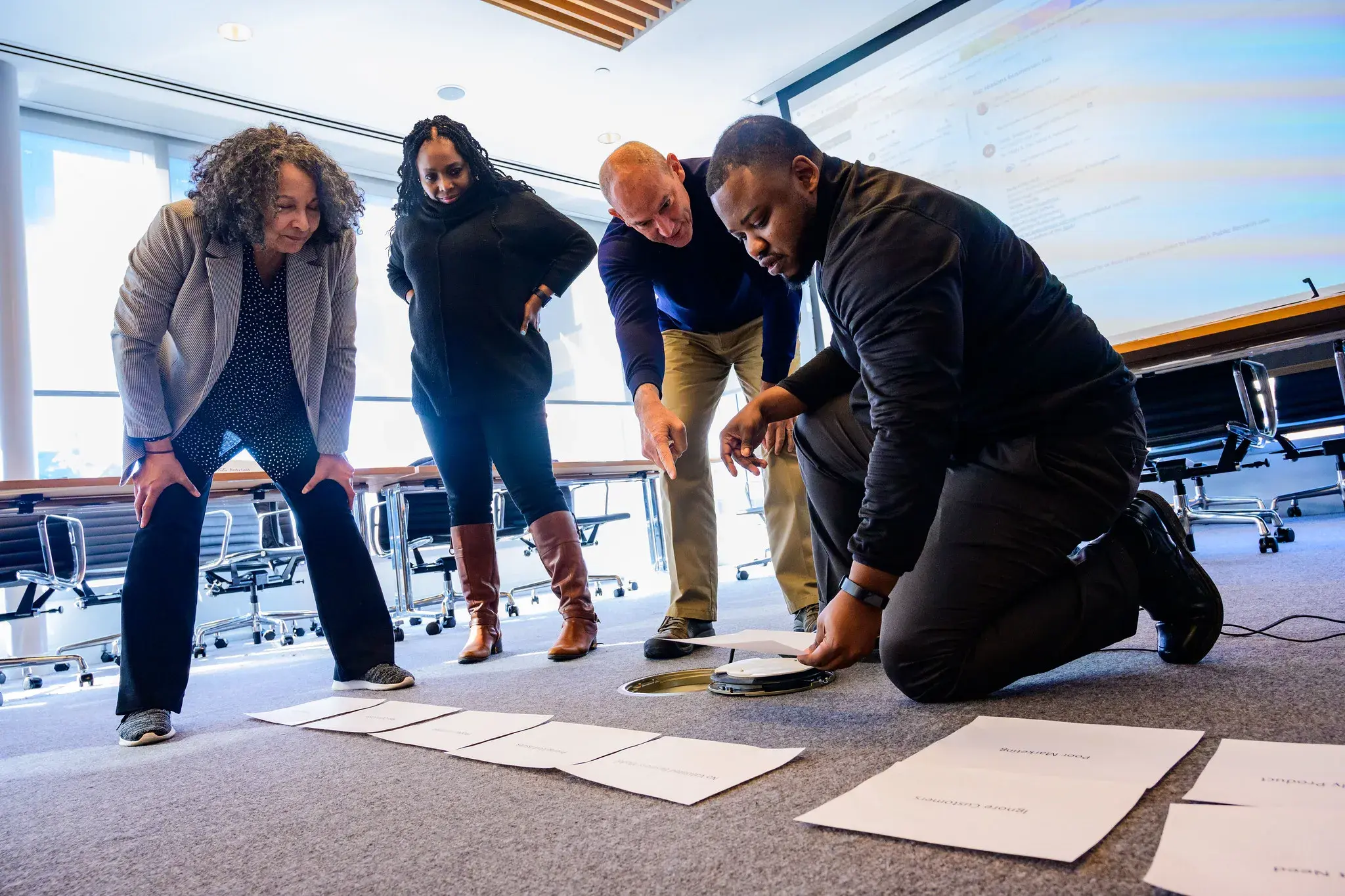 A group of 4 STRIVE participants gather around a spread of papers on the floor. One man kneels while the others bend over looking at the papers.