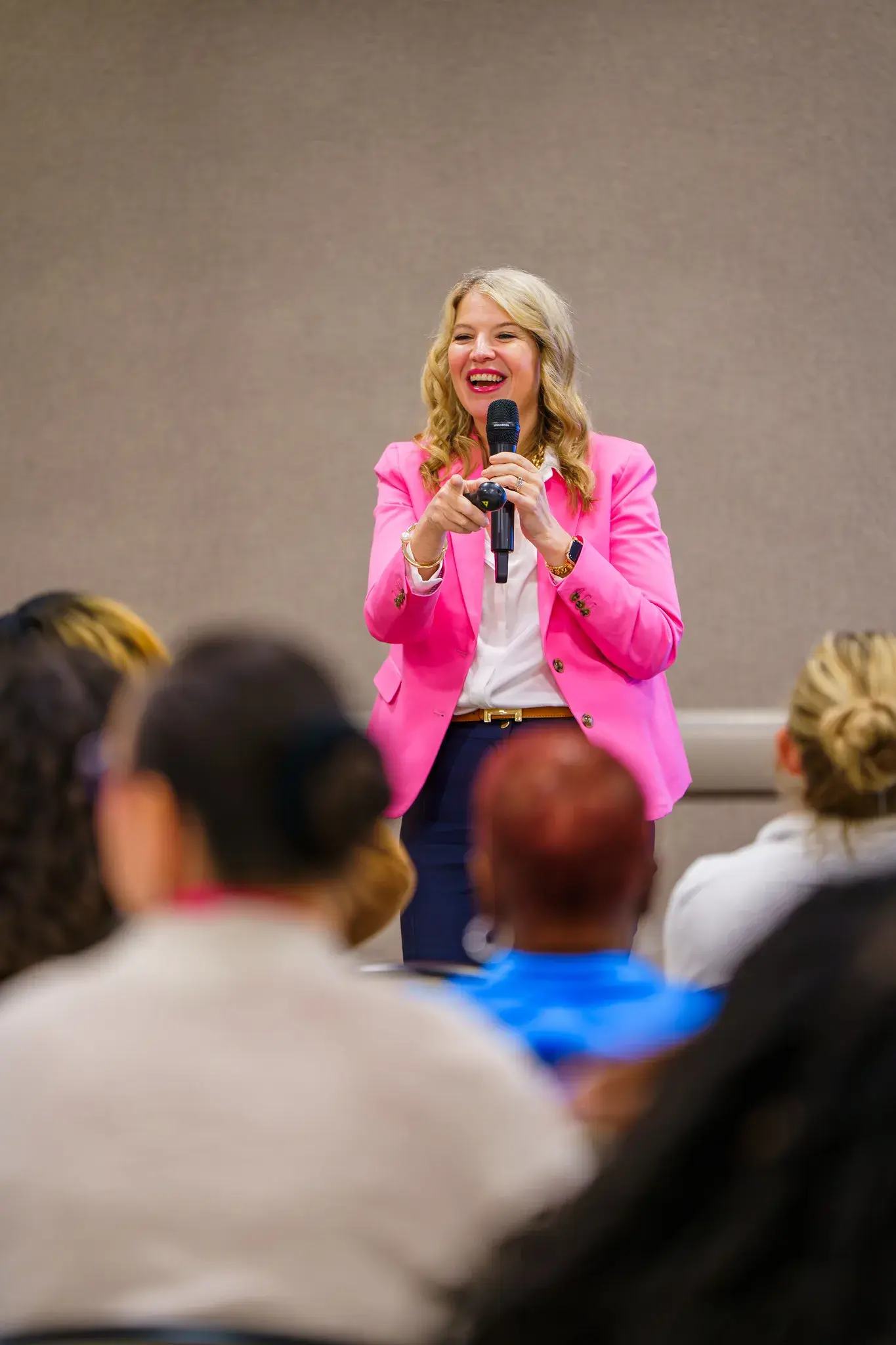 A woman in a blazer holds a mic and and gestures while addressing a crowded classroom in front of her at V-WISE Atlanta.