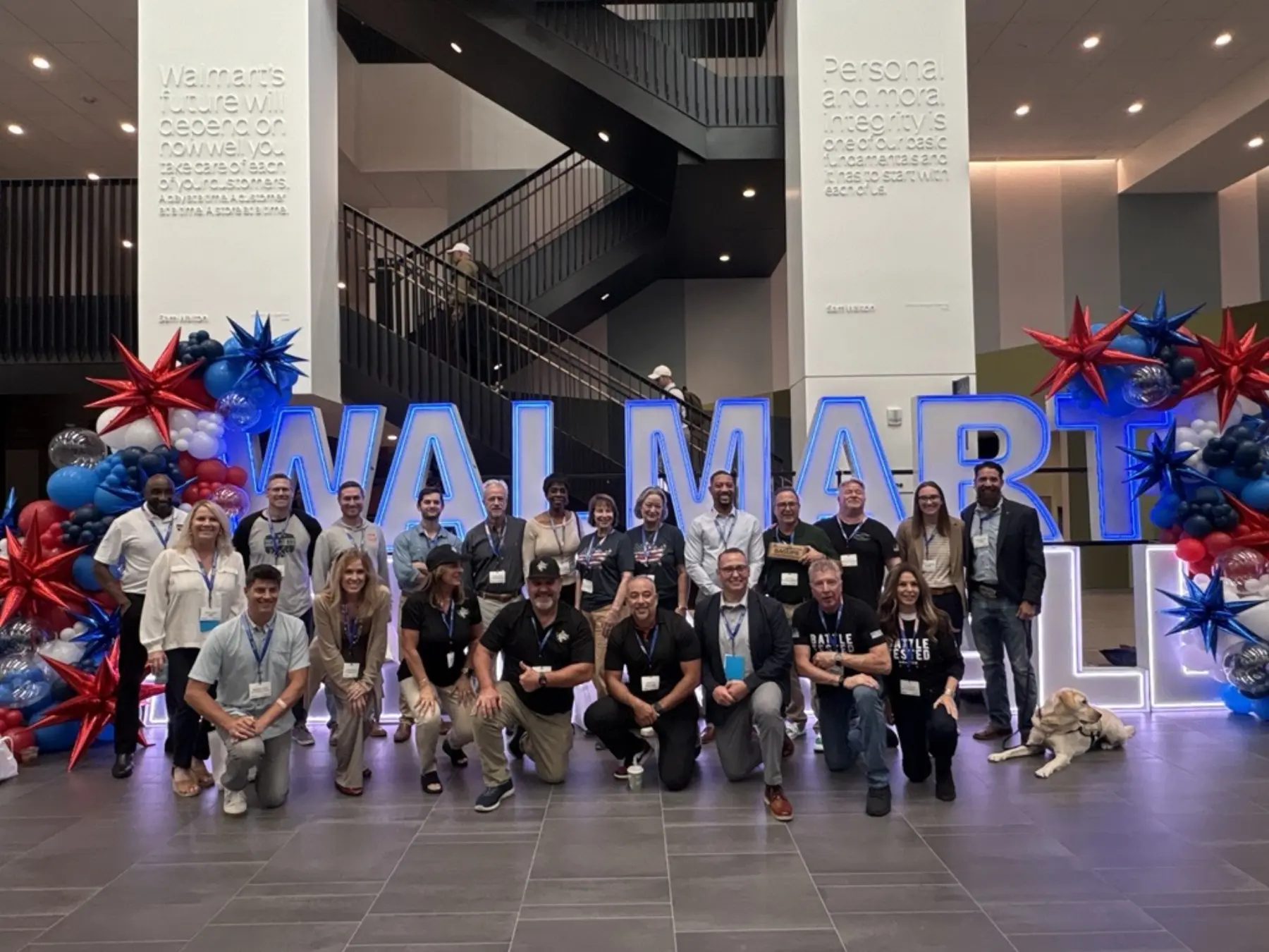 Group of Walmart Open Call attendees and a service dog in a large open area in front of a stack of large lighted letters spelling Walmart Open Call.