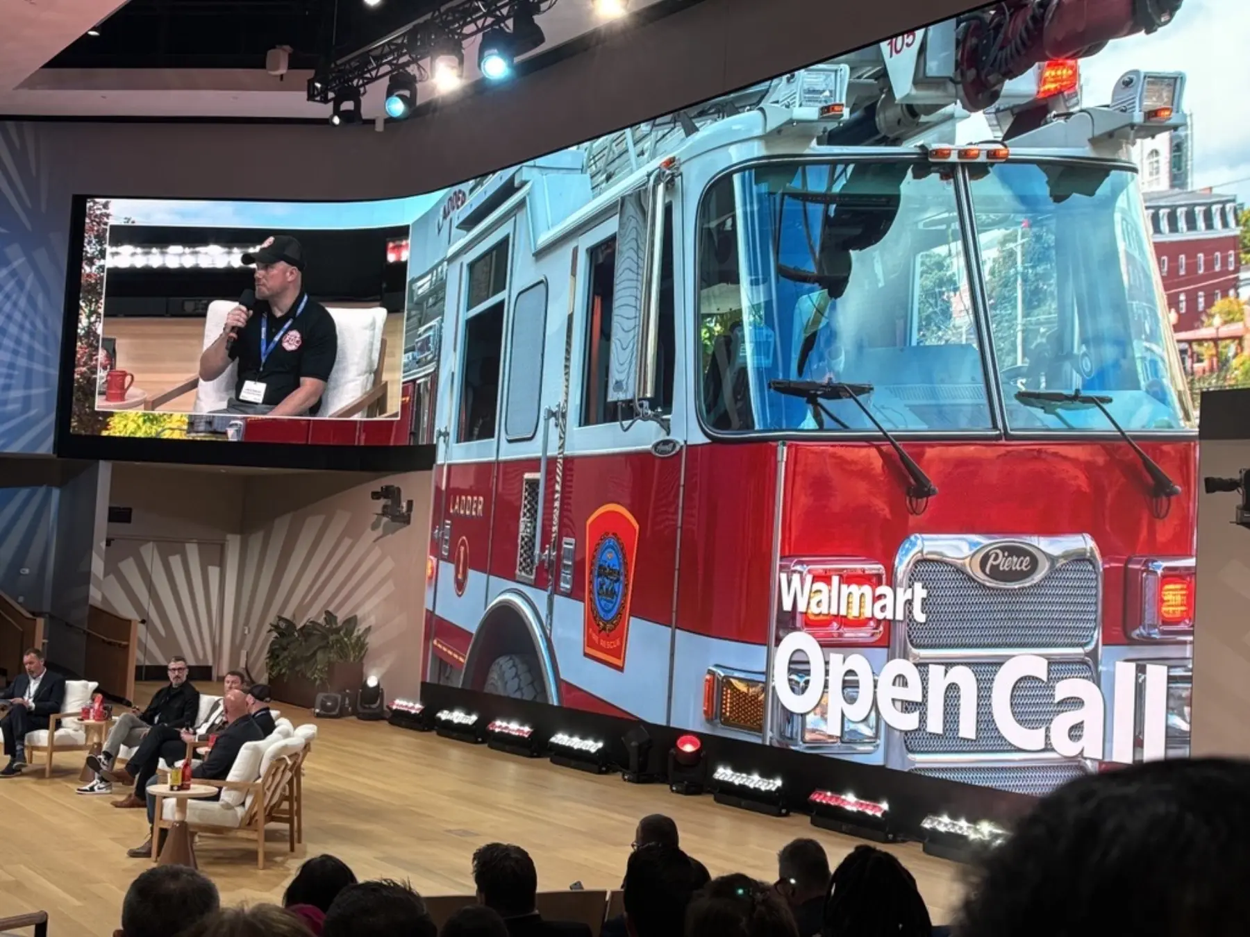 A large digital display on a stage behind panelists shows a firetruck and "Walmart Open Call" alongside a picture in picture close-up of a panelist.