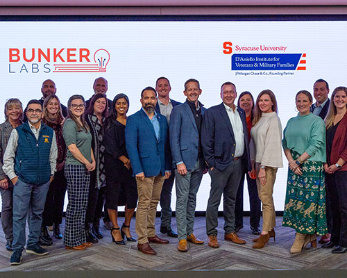 Group of people pose in front of a wall displaying logos for Bunker Labs and IVMF.