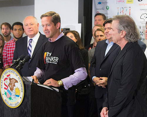 Todd Conner speaks from behind a podium, surrounded by people.