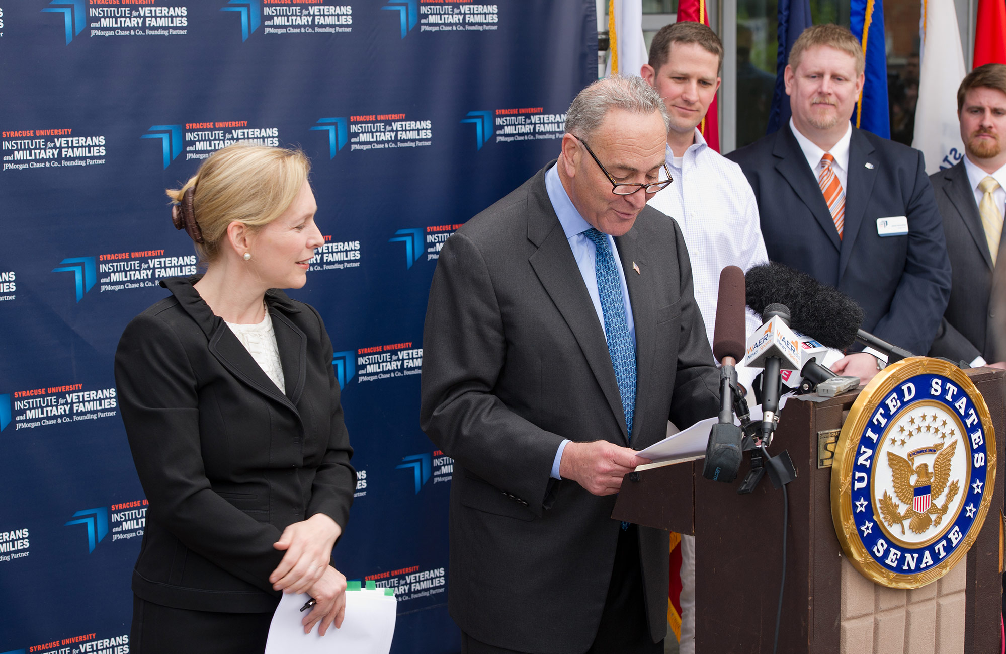 Chuck Shumur stands at a podium in front of a banner for IVMF
