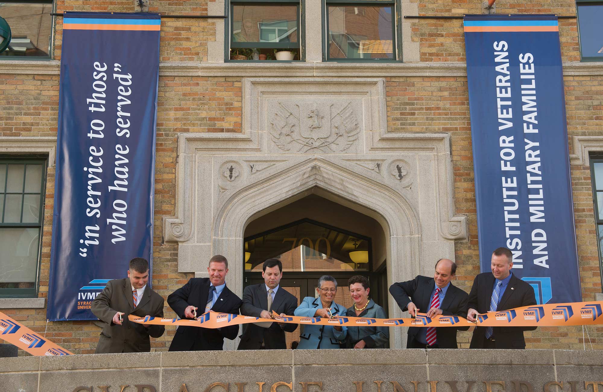 A group of people standing outside a university building while one person cuts a ribbon.