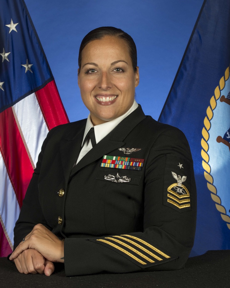 Leah Stiles in her military dress uniform posing for her headshot with two flags in the background.