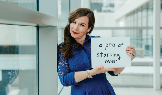 Military spouse leaning against glass and holding a sign that reads "a pro at starting over"