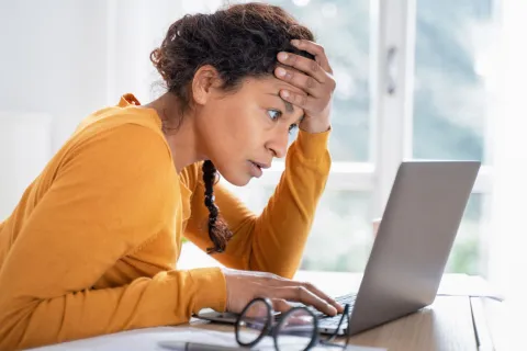 Woman looking stressed at an open laptop.