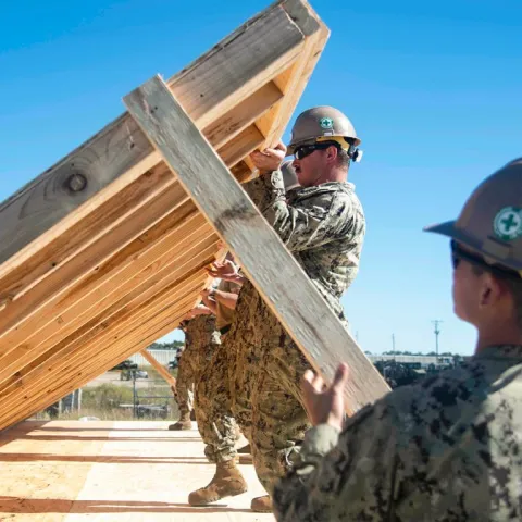 Soldier lifting up wood structure for building.