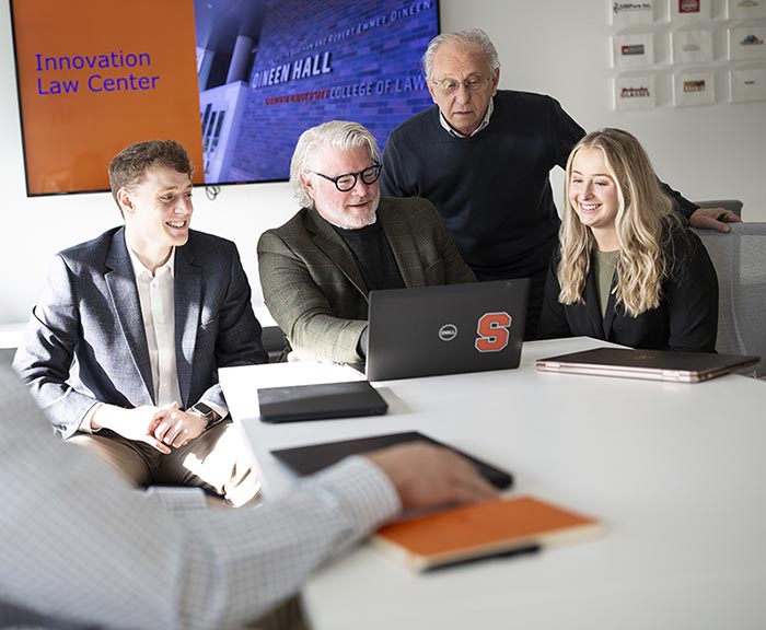 Two professors and two students work together in the Innovation Law Center, looking at a computer and smiling and talking together around a table.