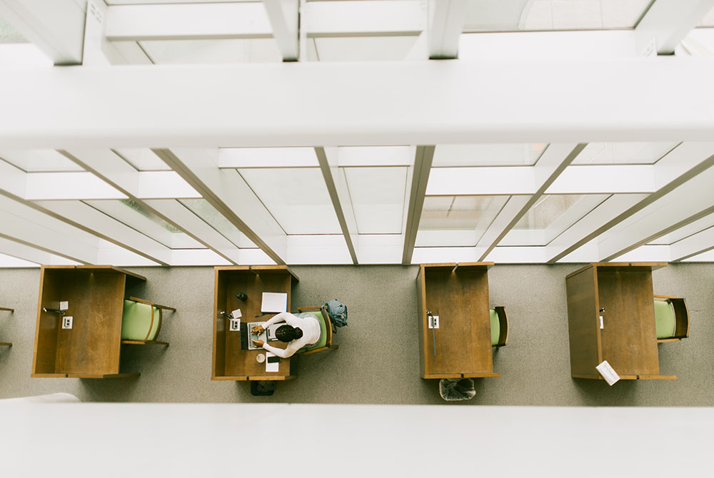 view from above four desks in the syracuse law library, with a student at the second to left desk doing work from an aerial view.