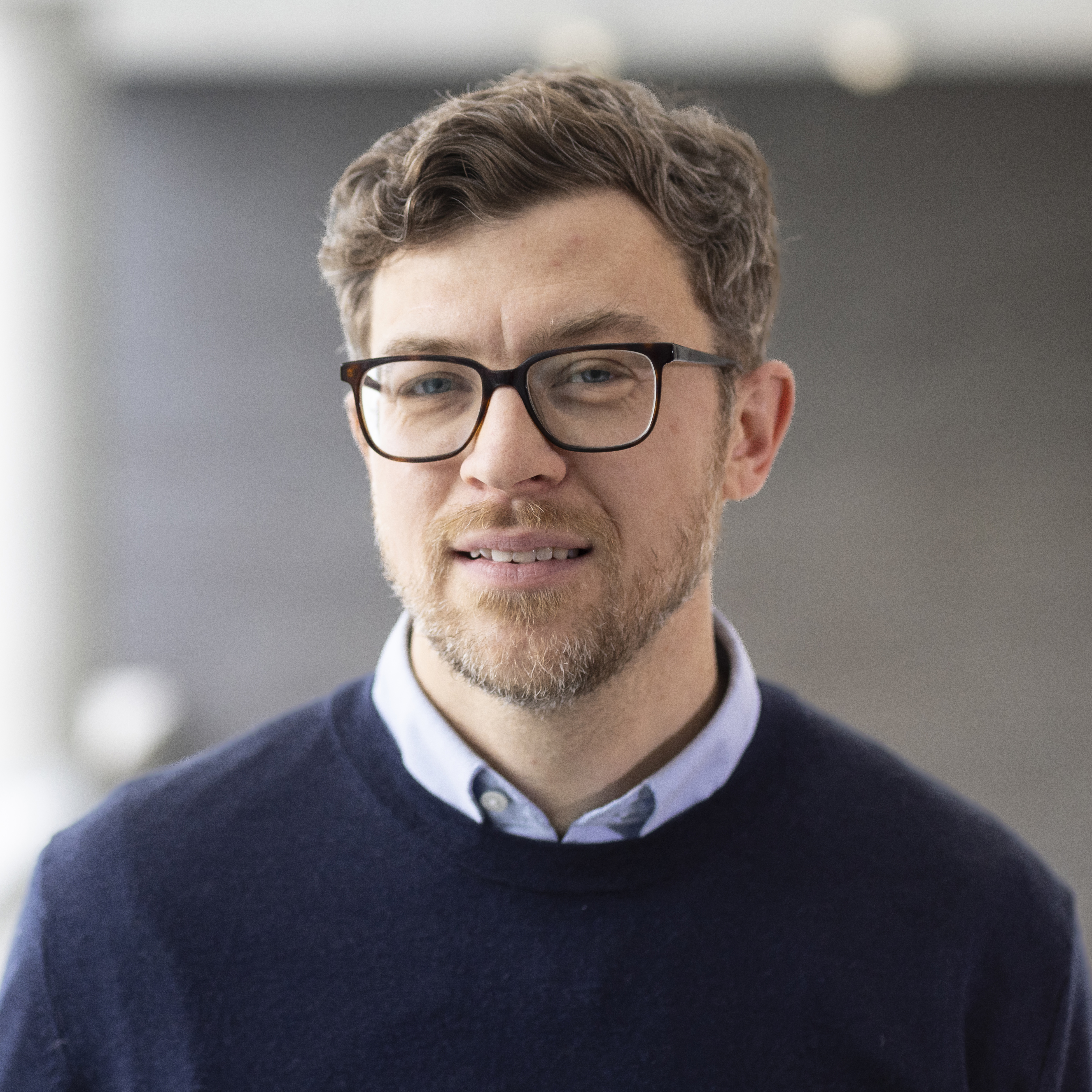 Headshot of Casey Weissman wearing a blue sweater in front of a gray abstract background.
