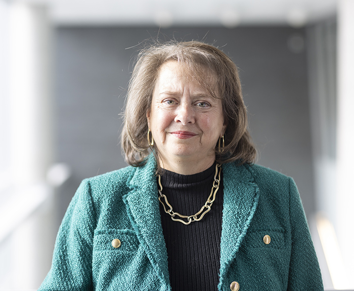 Headshot of Elizabeth August wearing a green blazer in front of a gray abstract background.