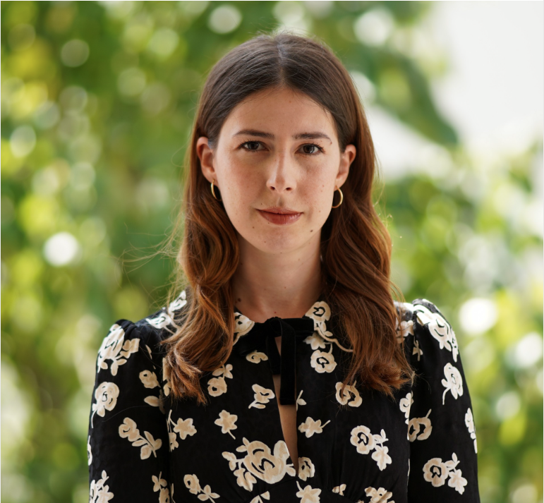 Headshot of Fitore Hyseni G&rsquo;24 wearing a black and white flowered blouse in front of greenery.