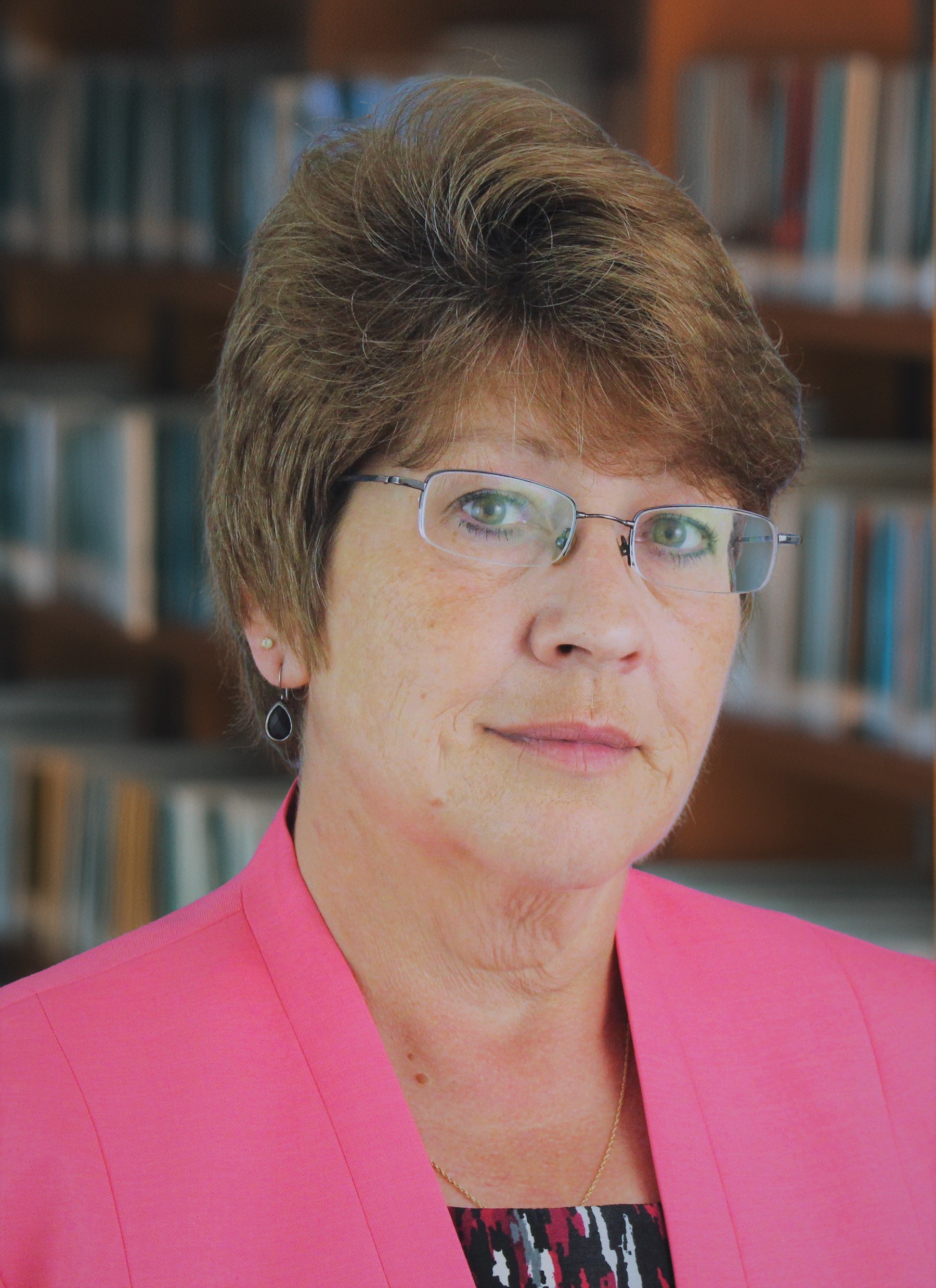 Headshot of Jan Fleckenstein wearing a pink blazer in front of a bookshelf of books.