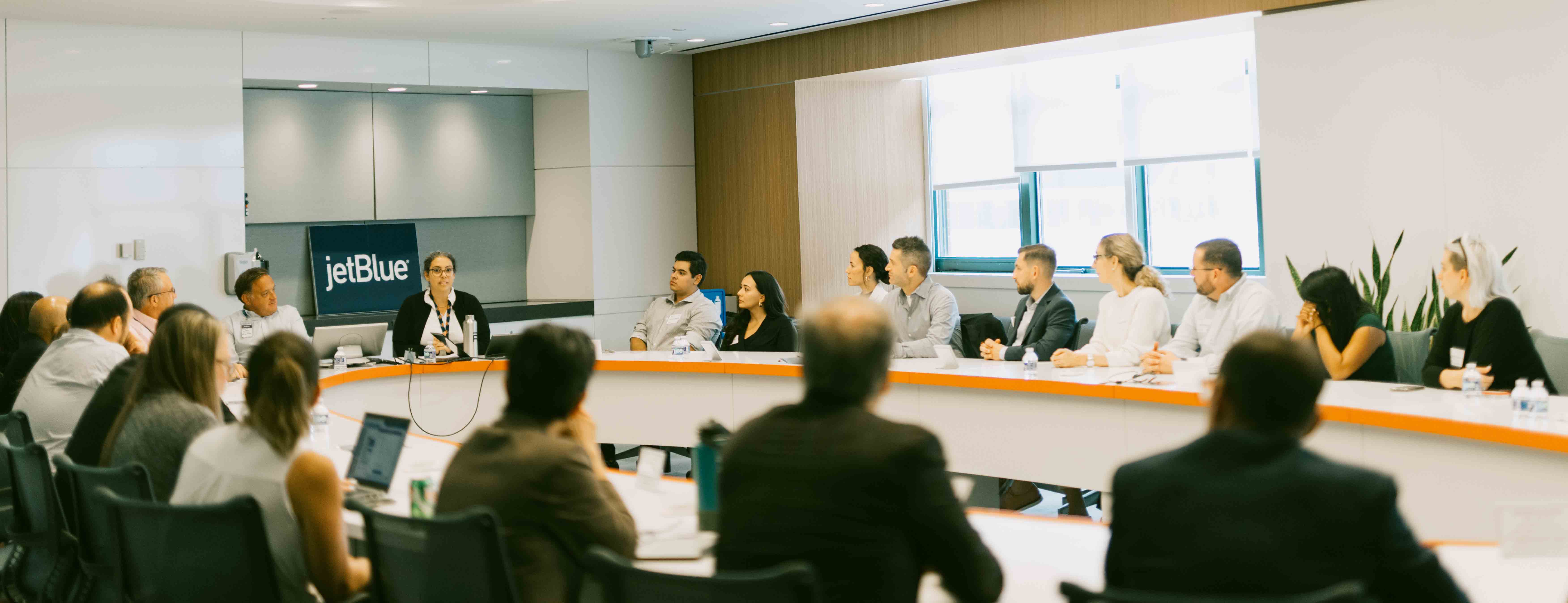 Students sit around the table at the JetBlue HQ in DC listening to the professor speak.