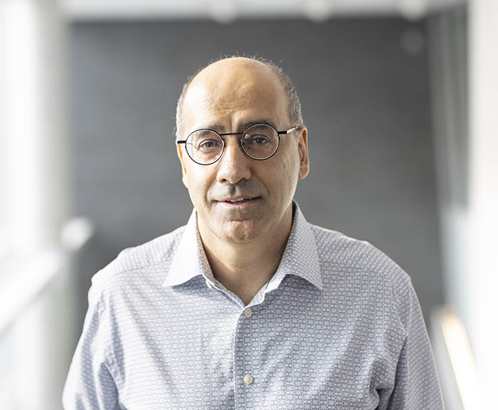Headshot of Rakesh Anand wearing a button down shirt in front of an abstract gray wall.