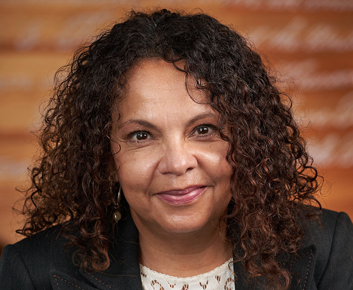 Headshot of Suzette Melendez in front of the college of law library wall