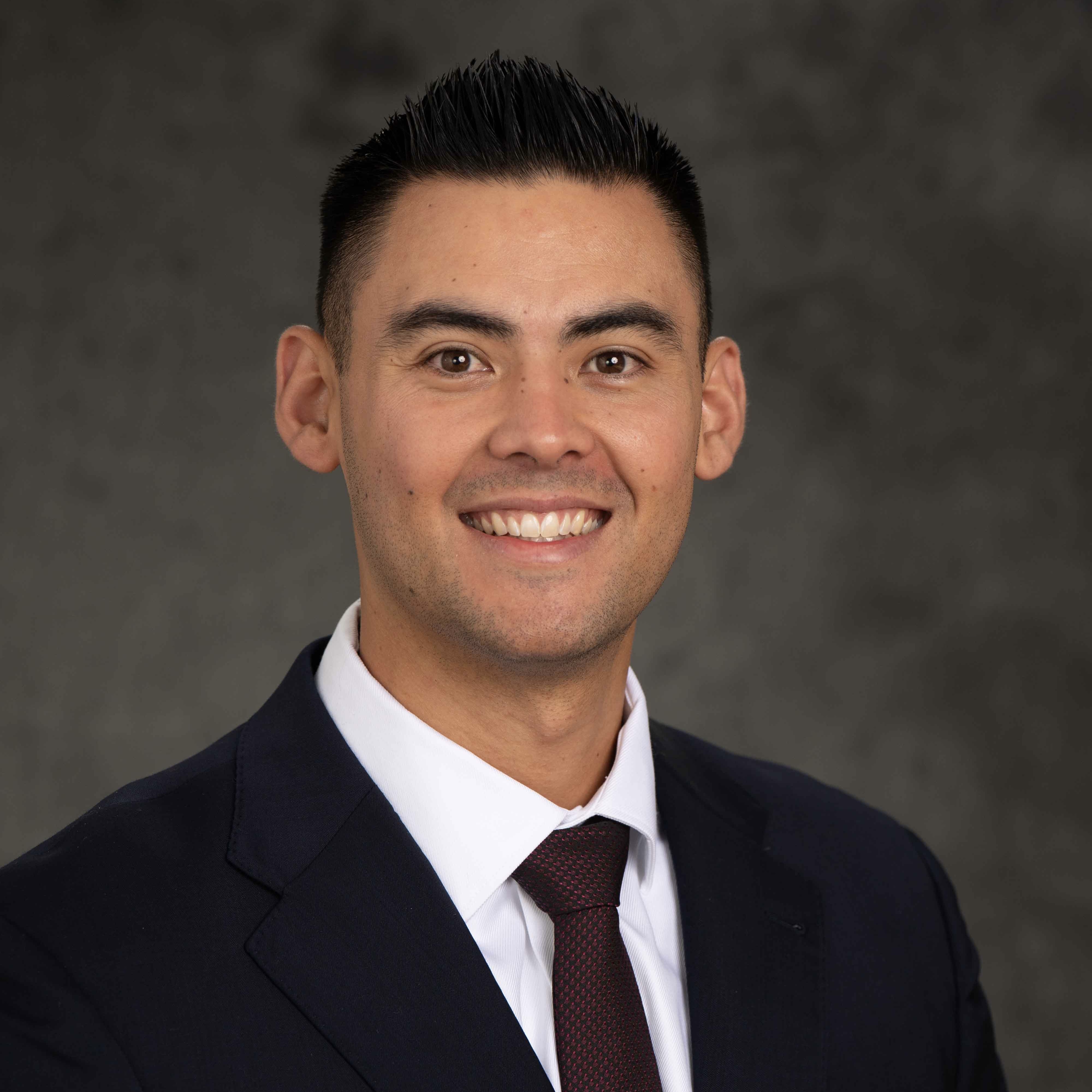 Jonathan Andrade wears a black suit in front of a gray background.