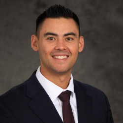 Jonathan Andrade wears a black suit in front of a gray background.
