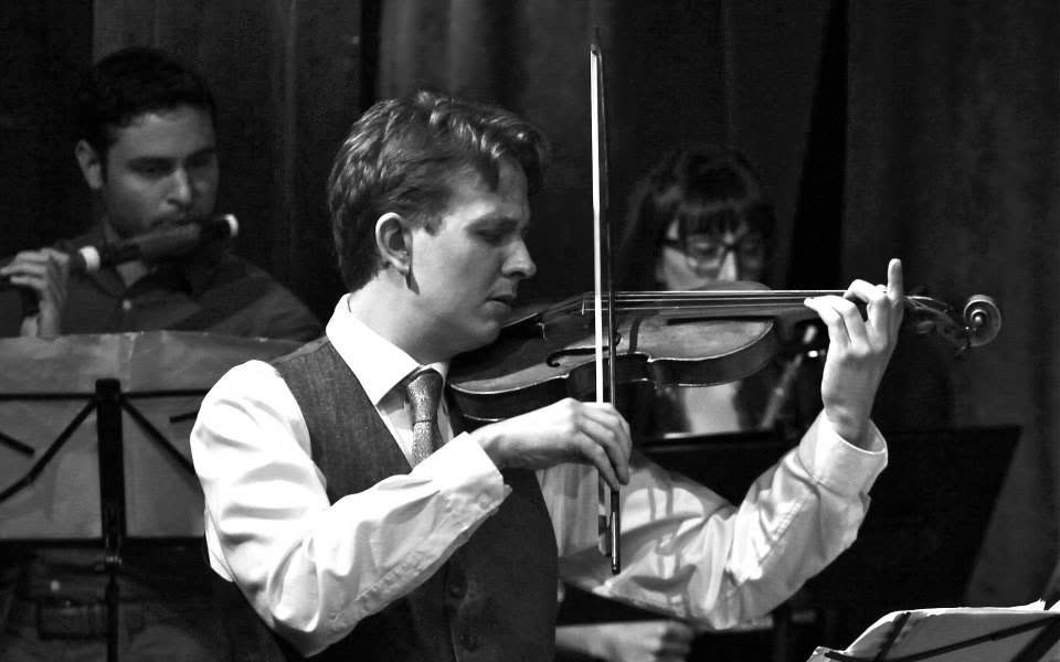 Jude Ziliak plays the violin in a concert on stage wearing a white button down.