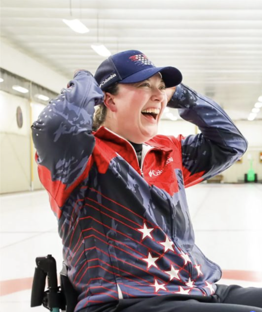 Katie Verderber sitting in wheelchair on ice rink wearing TEAM USA jacket.