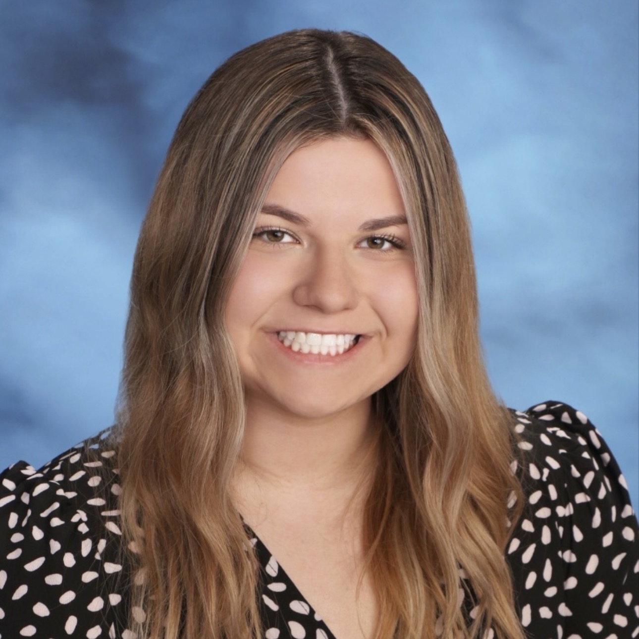 Maggie Clancy wears a pattern shirt in front of a blue background.