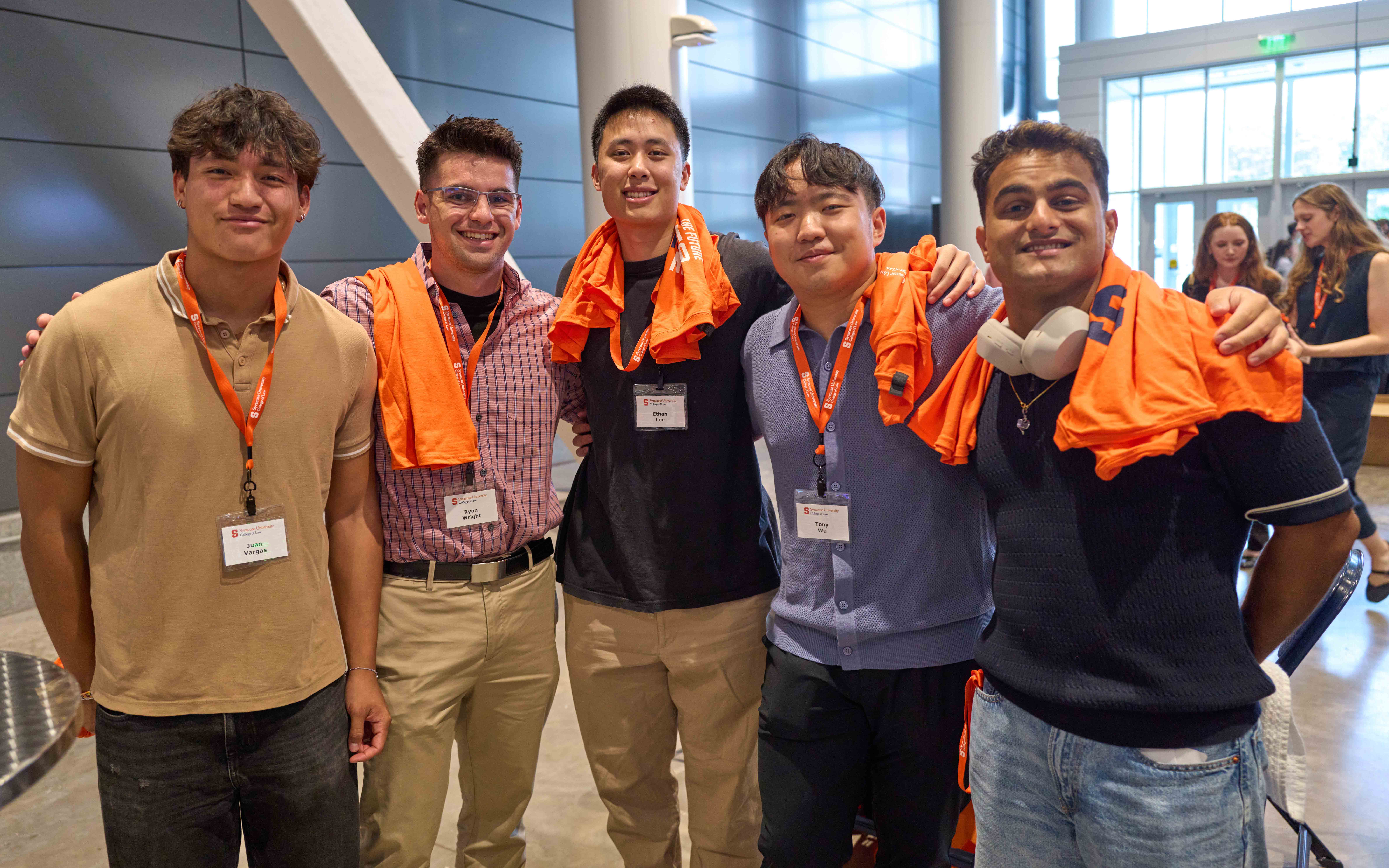 Group of five incoming students stands with their orange shirts and arms around each other.