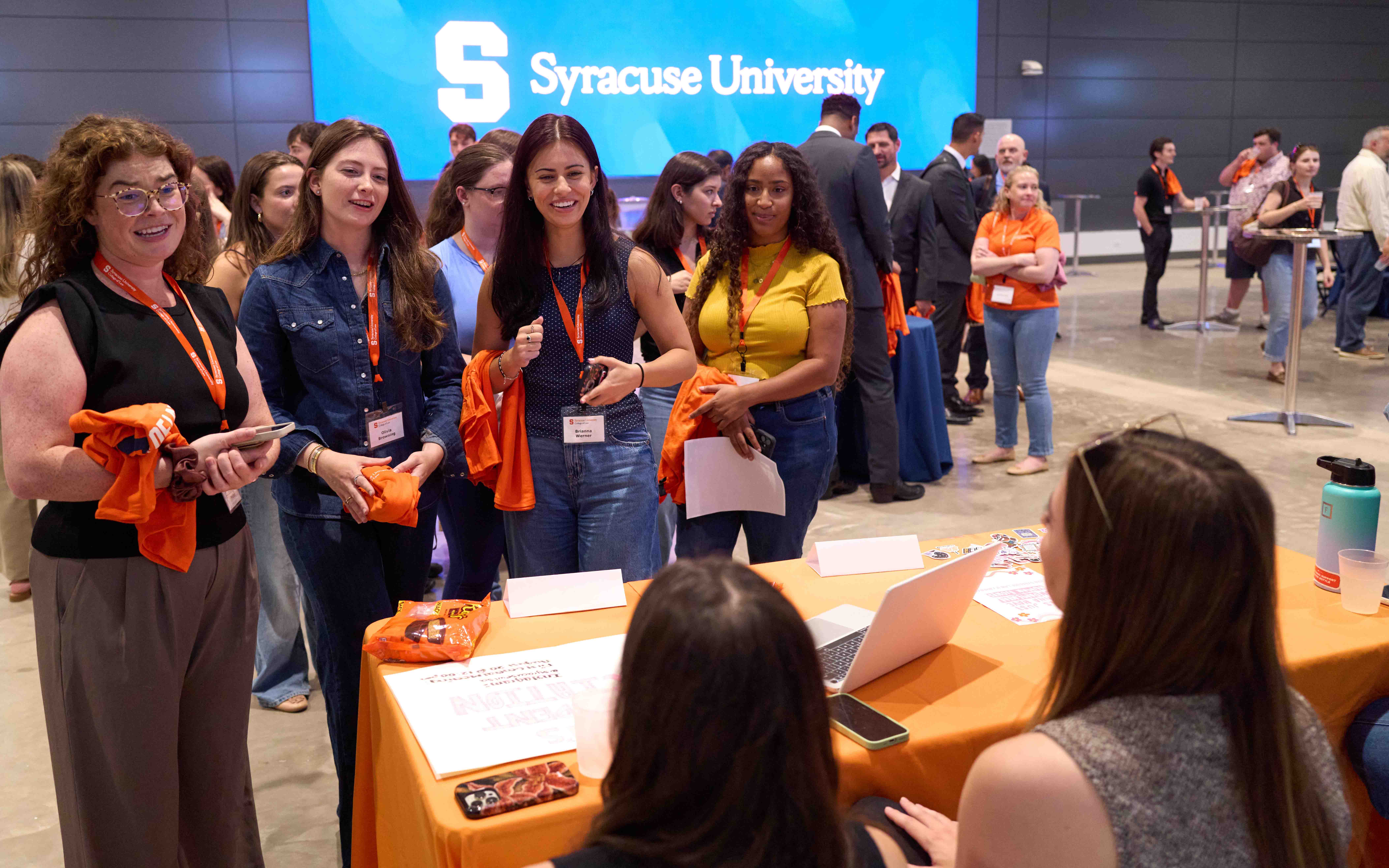 Four students stand at a student org booth and talk to two students who are sitting to welcome.