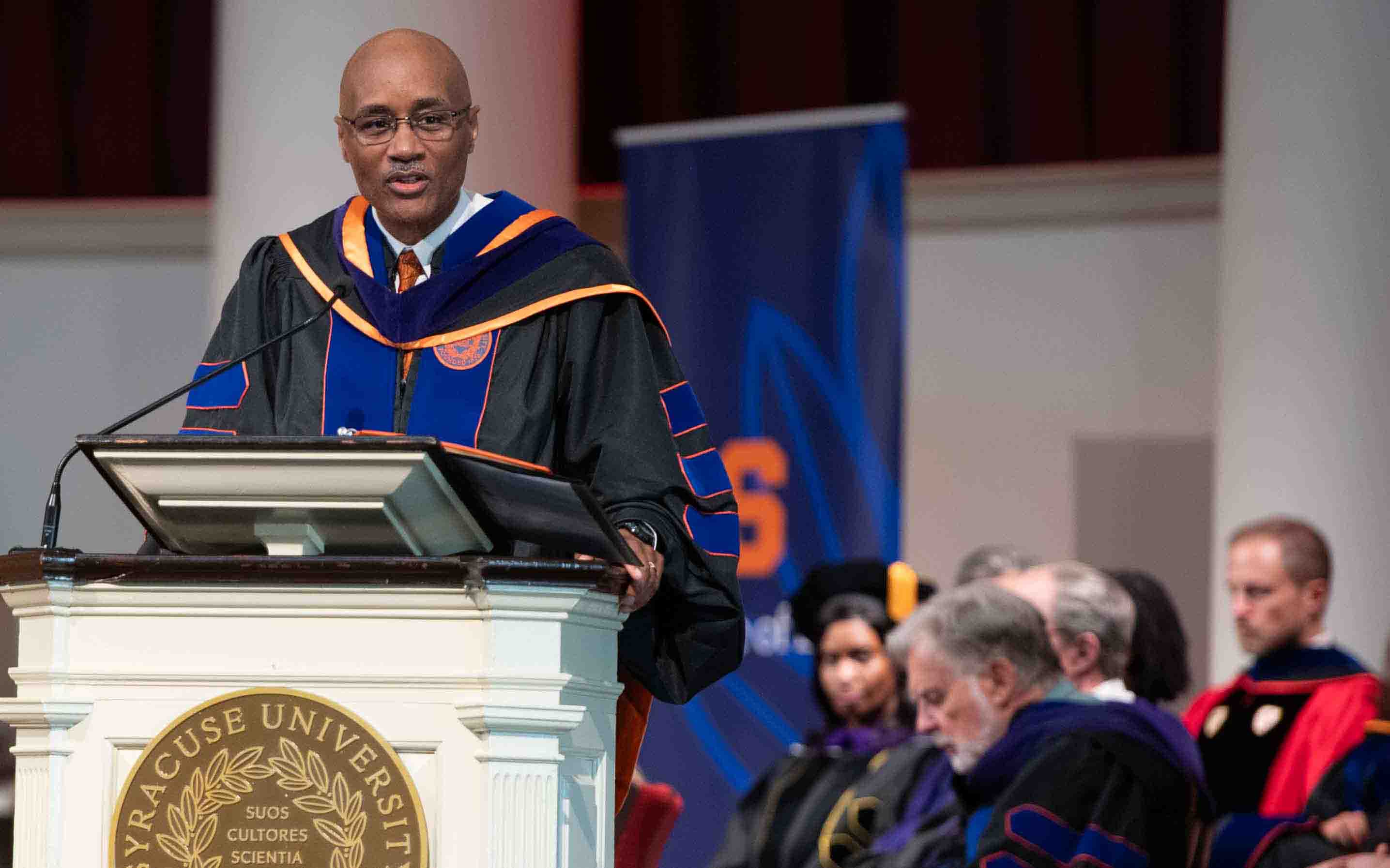 Convocation speaker speaks from the podium wearing a robe at Opening Convocation.