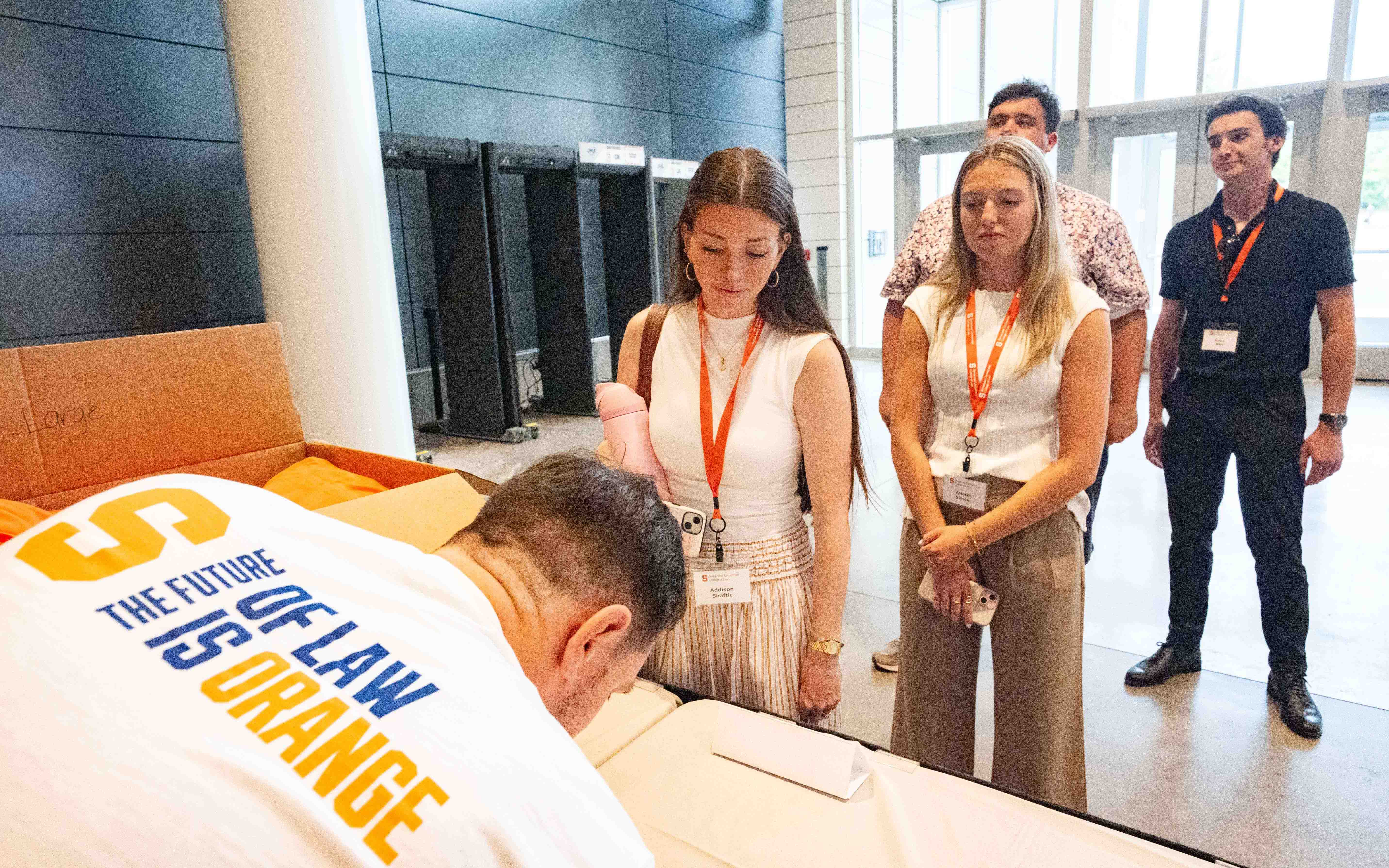 Four students come to check in at a table where a staff member wears a white future of law shirt.