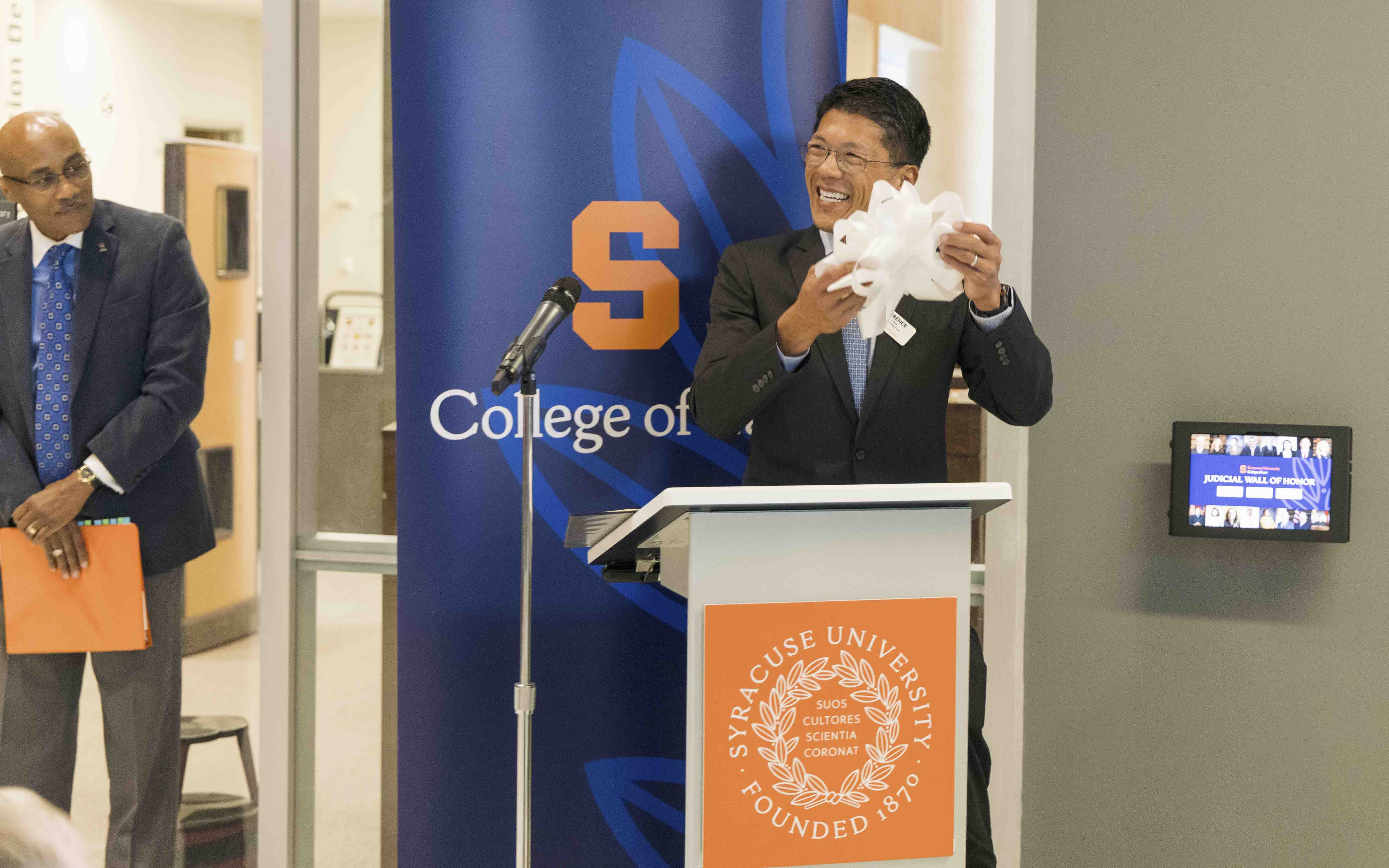 Dean Lau takes the ribbon off of the screen for the Judicial Wall of Honor, standing behind a podium.