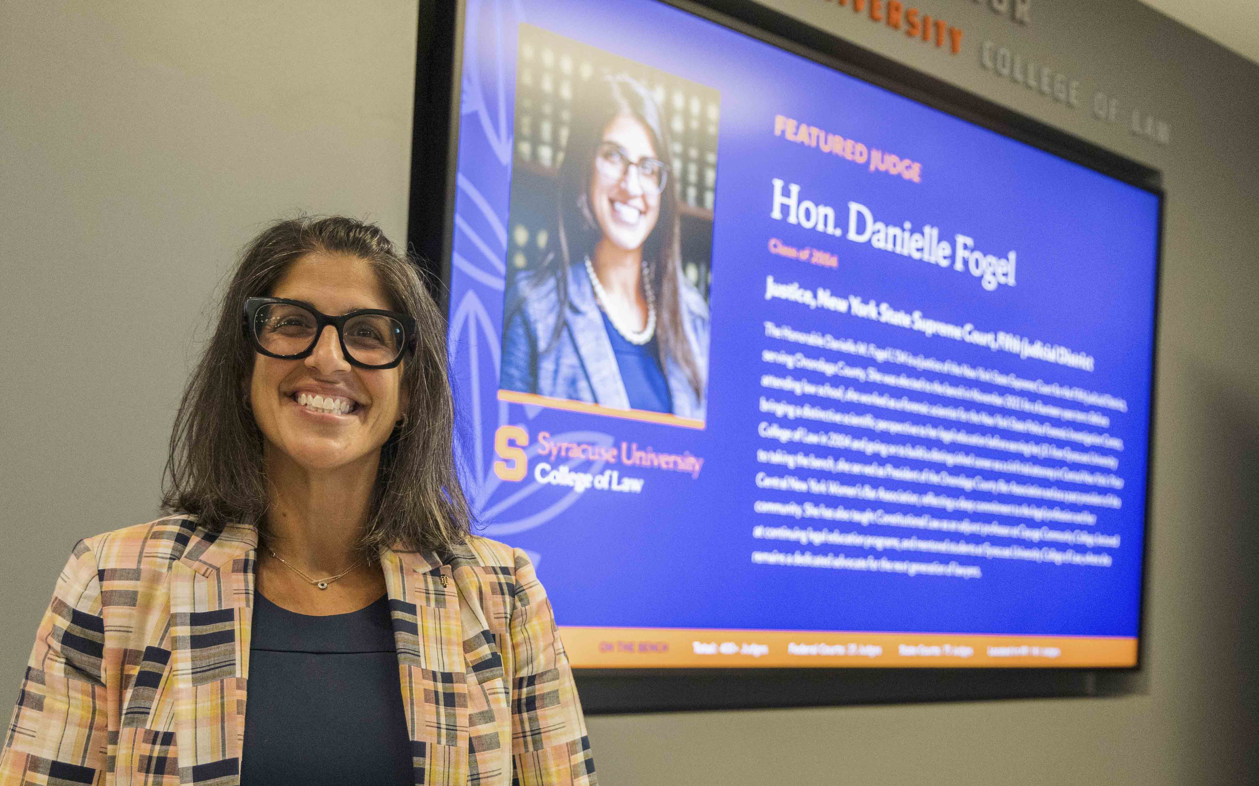 The Hon. Danielle Fogel stands in front of her Judicial Wall screen.