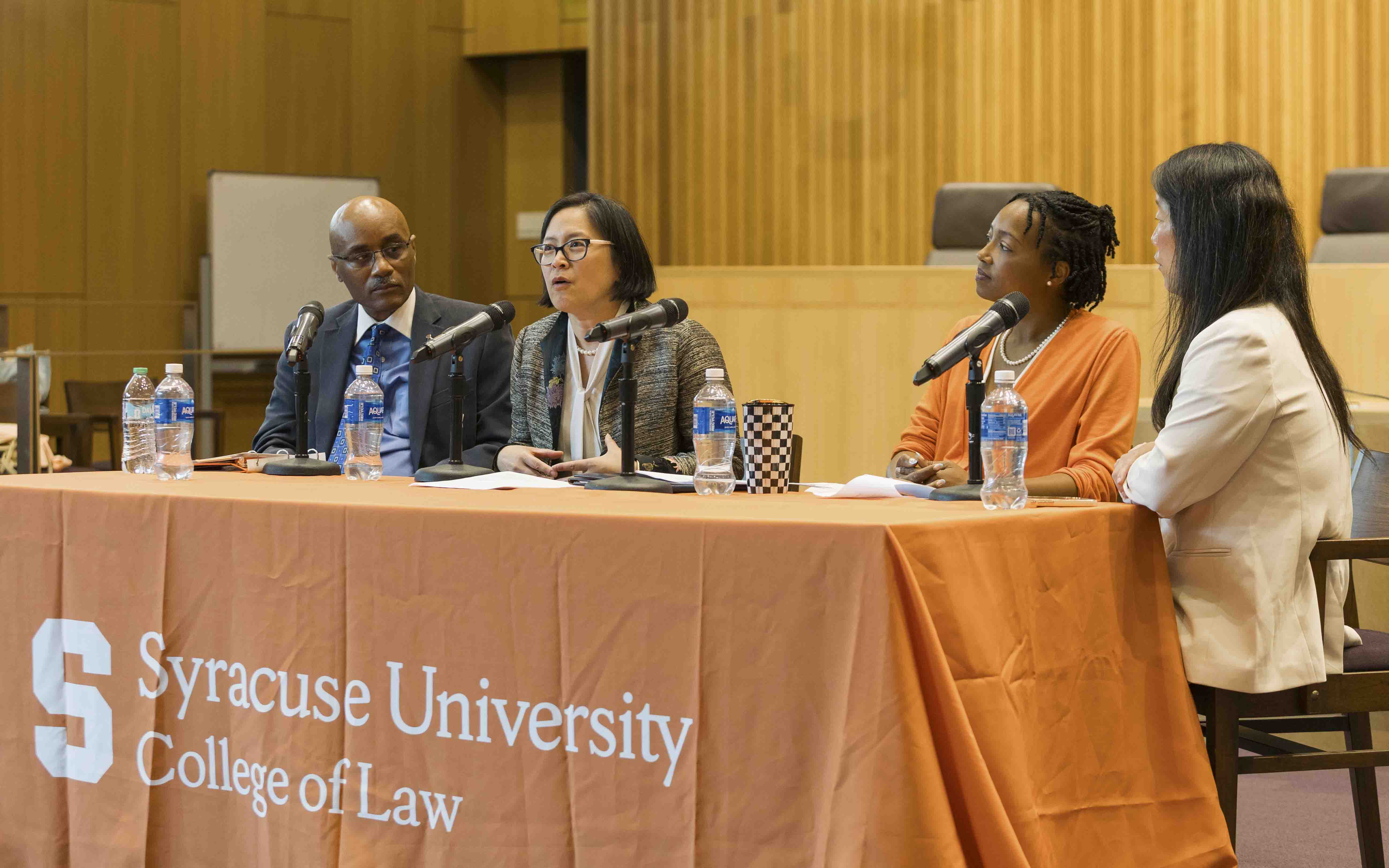 Four panelists sit behind a table with an orange Syracuse College of Law tablecloth speaking into microphones.