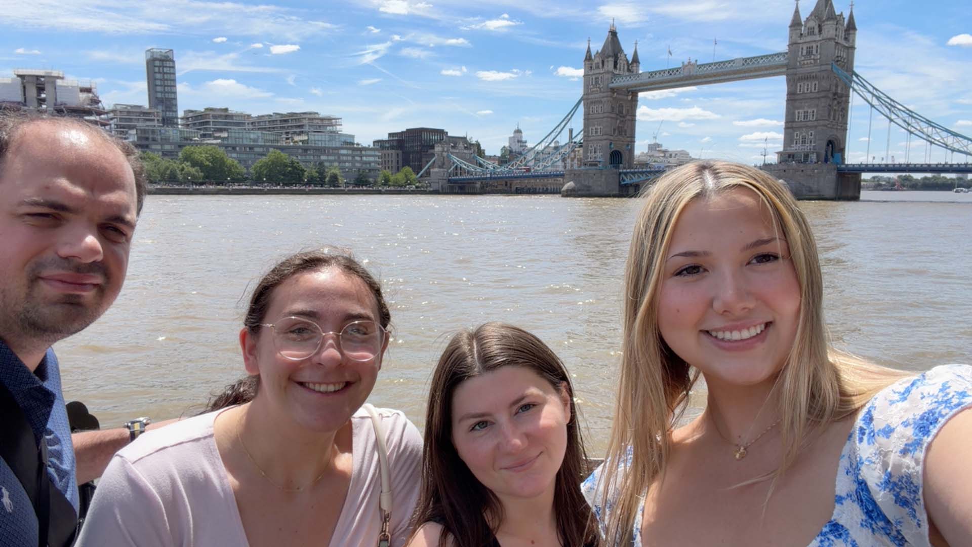 Four students pose for a selfie in front of a bridge and body of water in London.