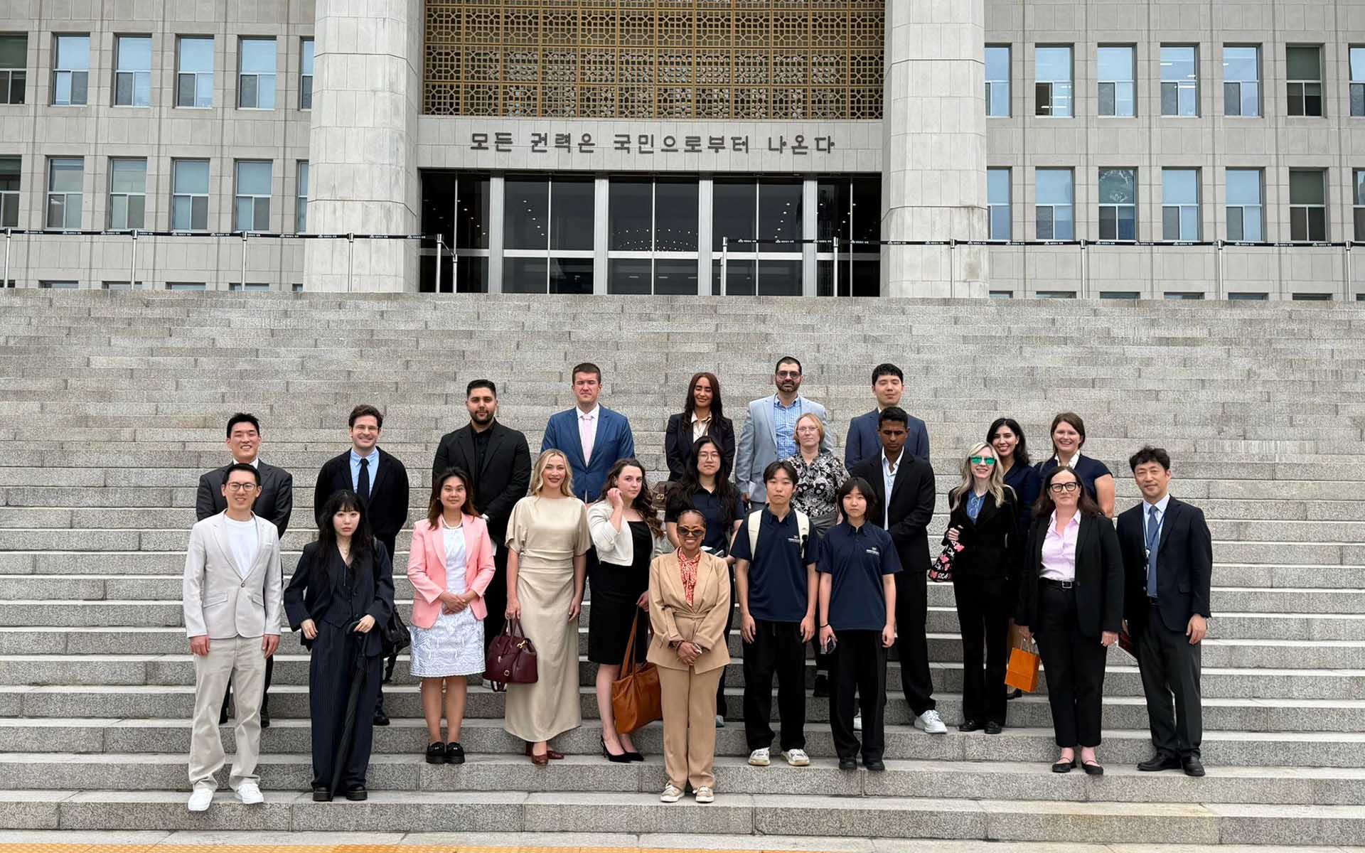 Group of about 20 students stands in front of the National Assembly of South Korea. 