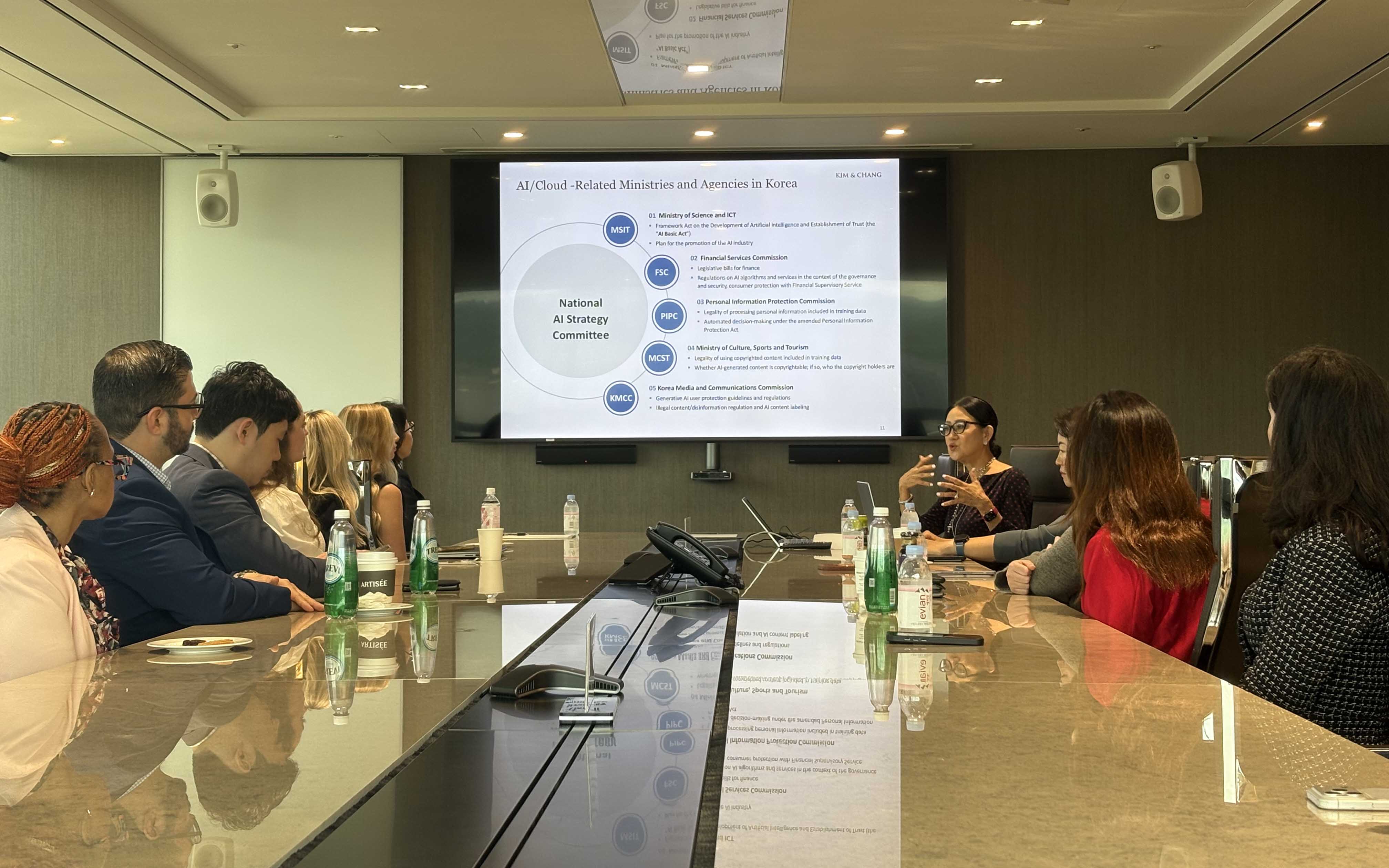 Students sit around a table looking at a screen with a presentation on the wall. 