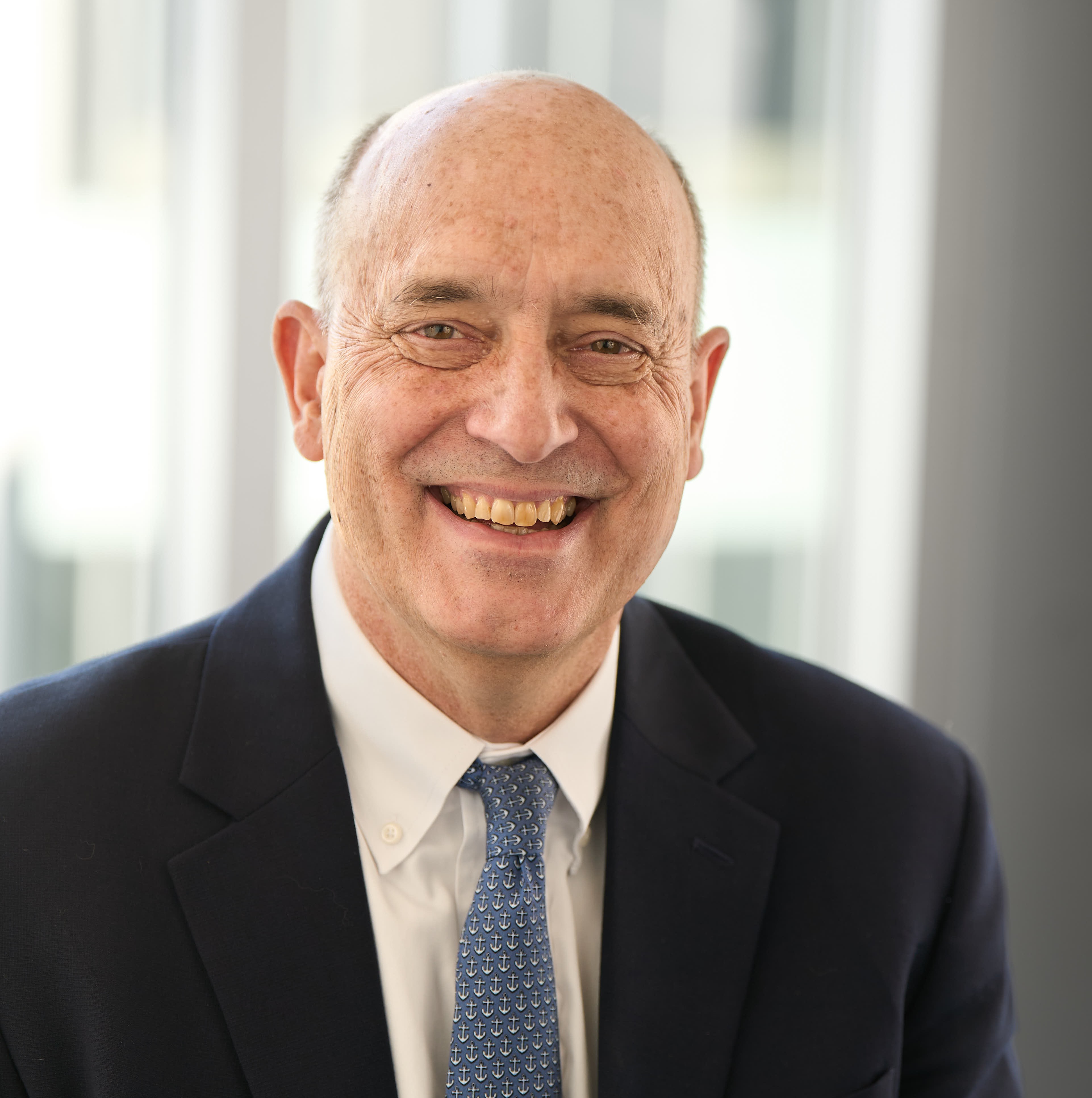 A man in a dark suit and blue tie smiling.