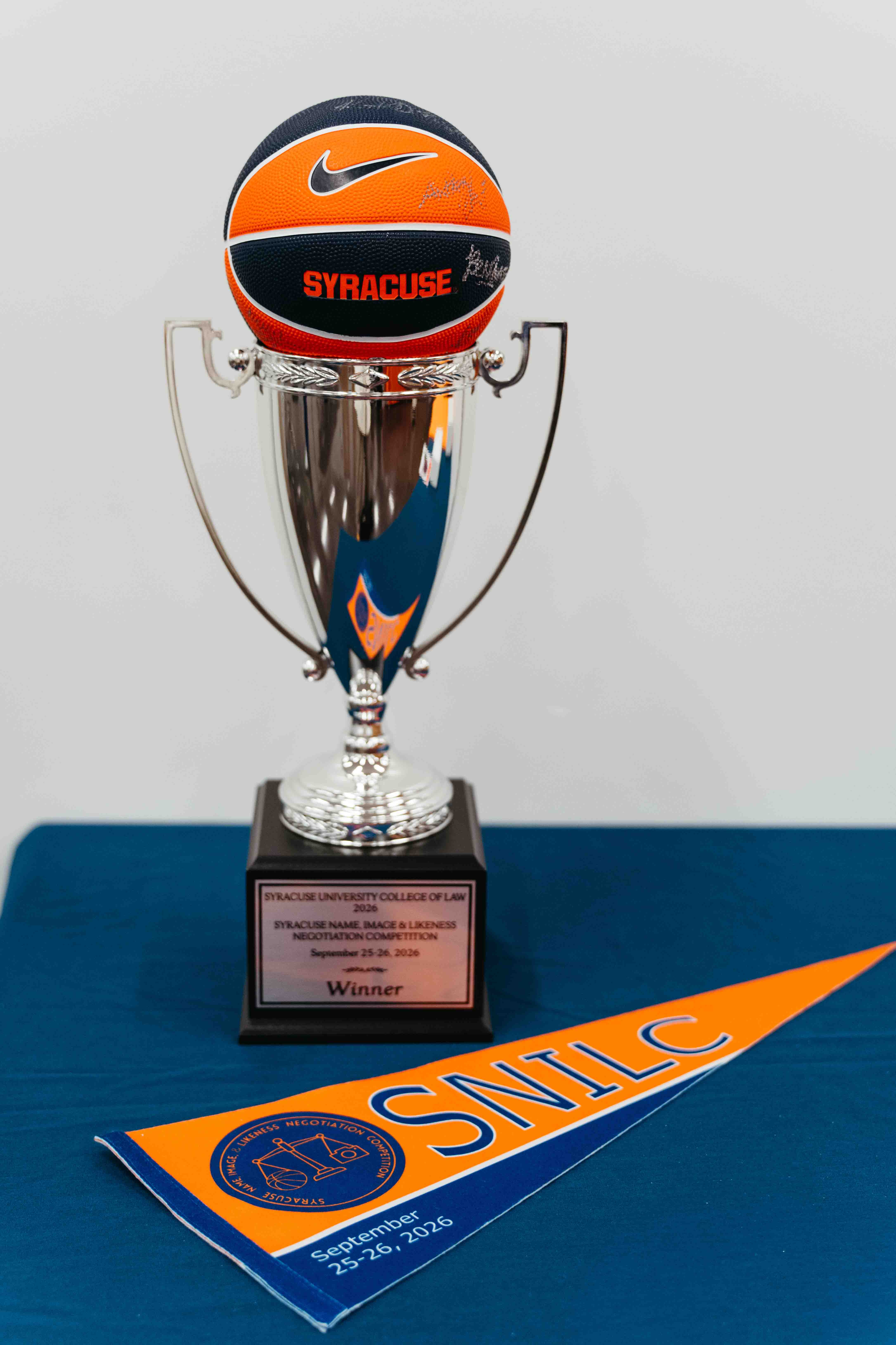 NIL Competition trophy with a basketball at the top, in front of an SNILC banner on a table.