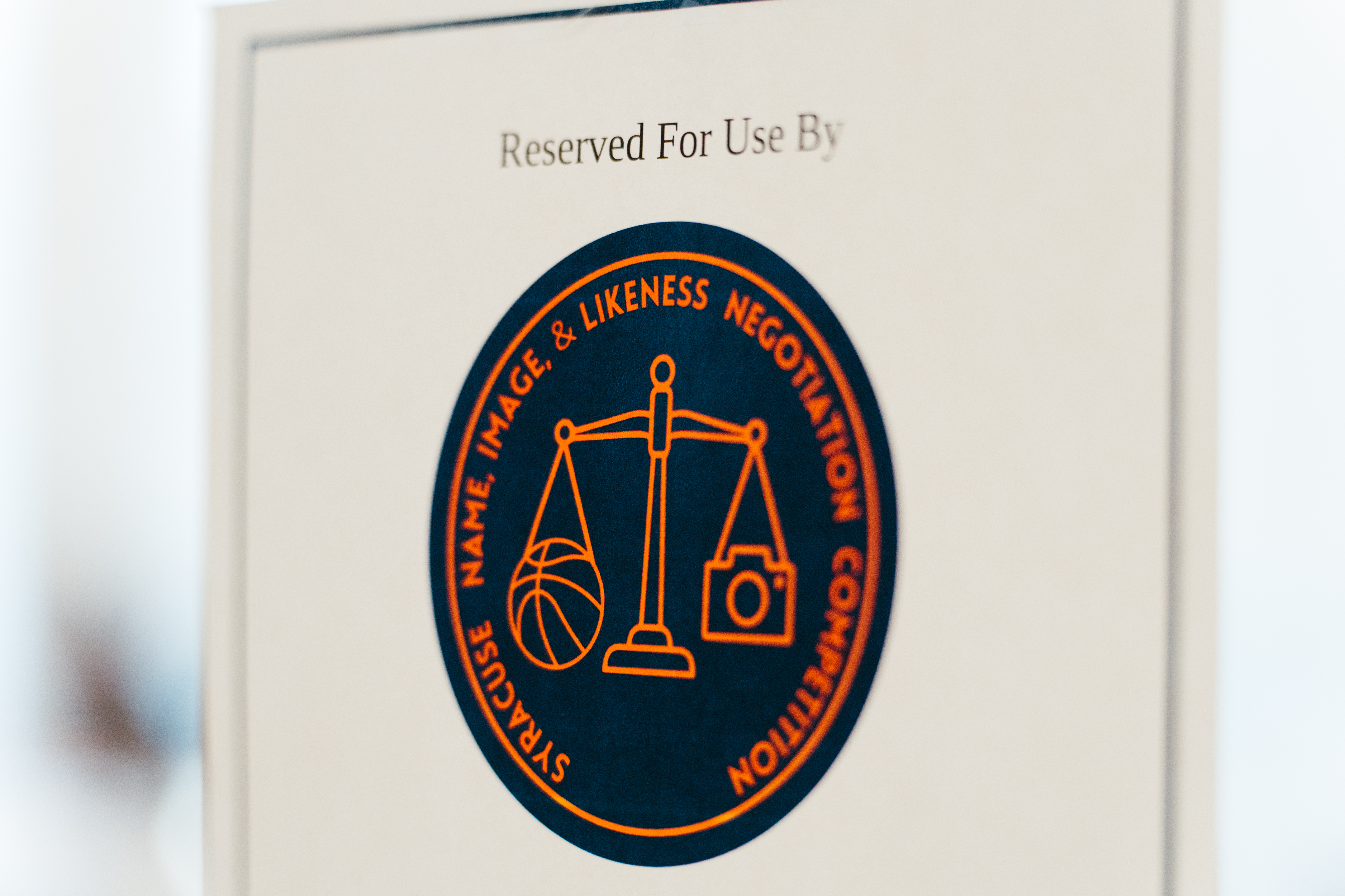 logo for the NIL competition in a circle on a pamphlet in orange and blue with justice scales.