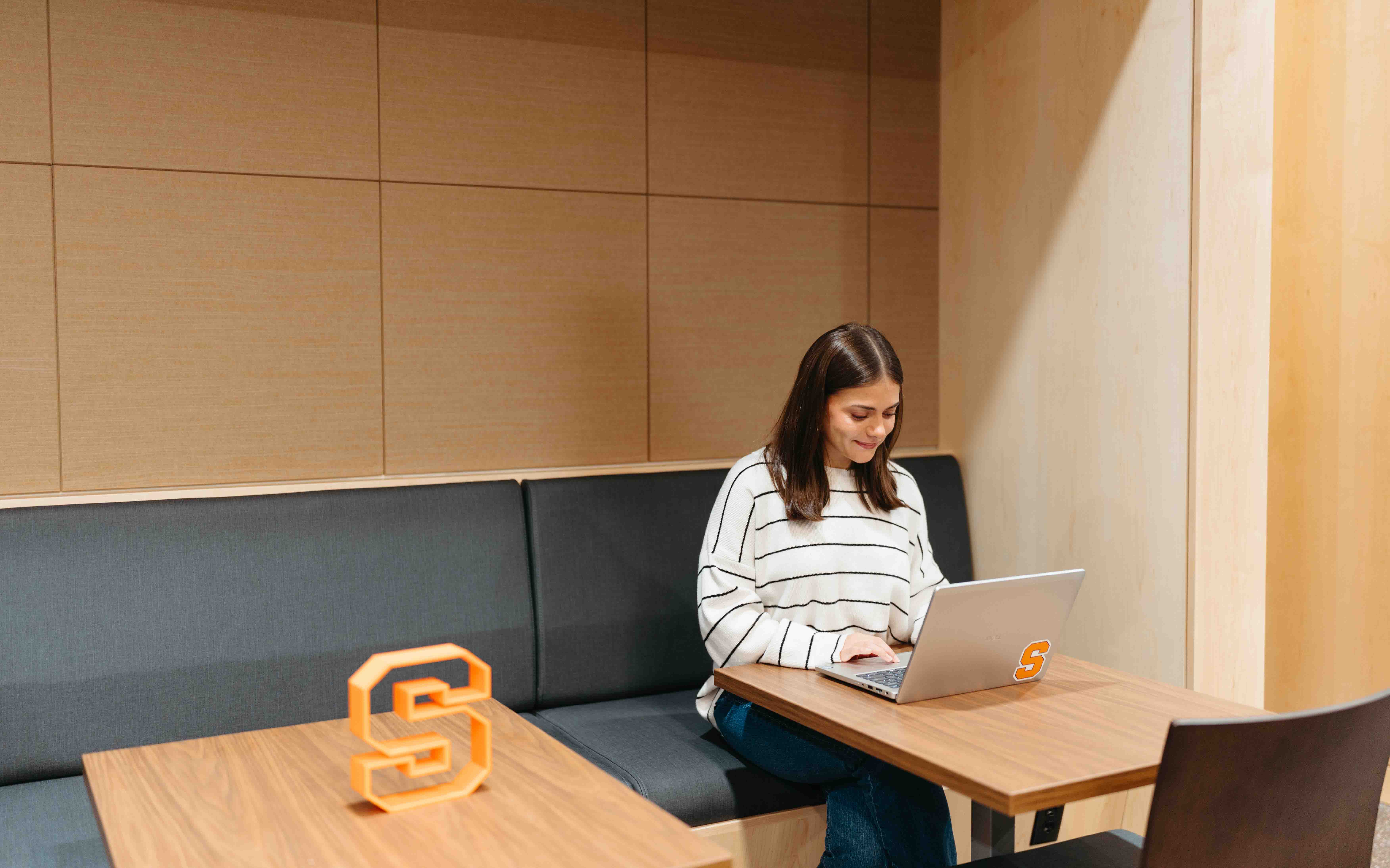Student works on computer at a space in the new student commons, sitting on a gray bench.
